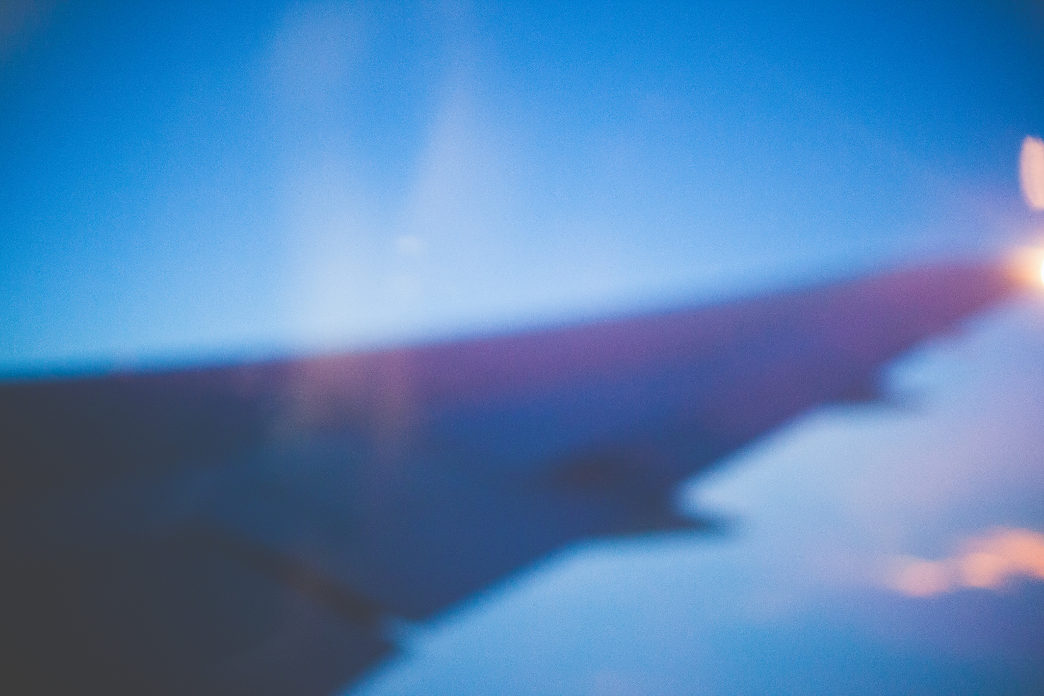 Dark silhouette of an airplane wing against a gradient twilight sky seen through a window.