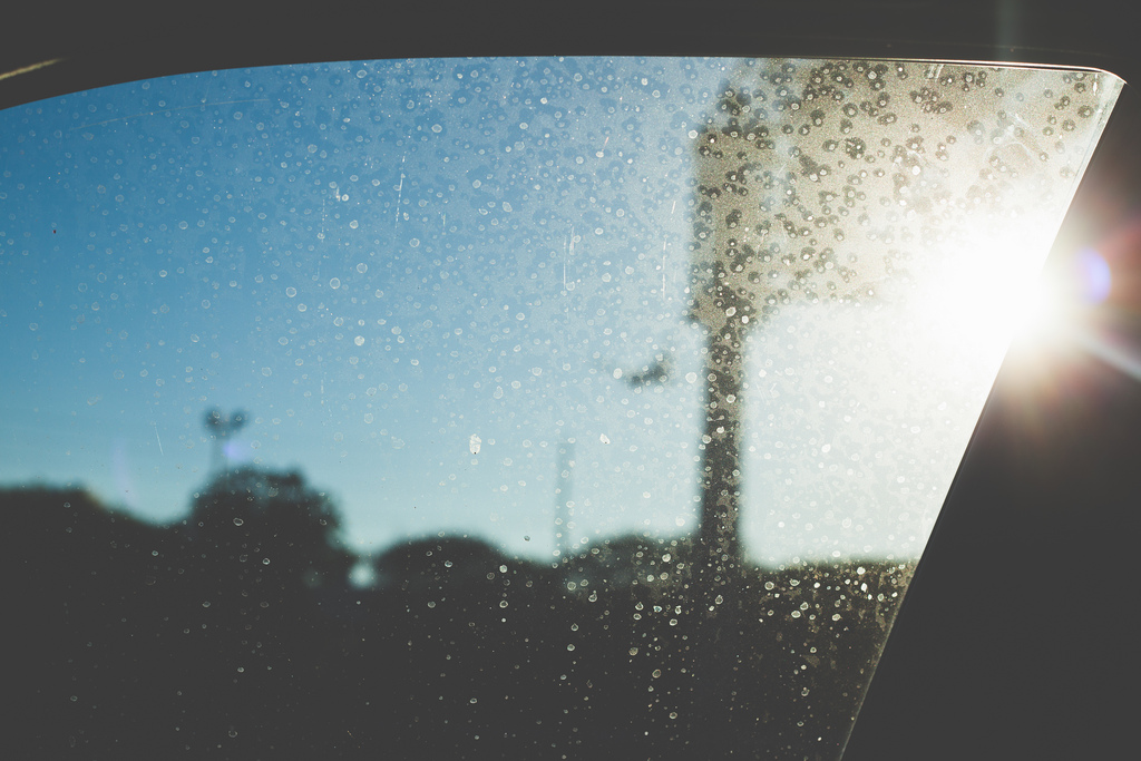 Sun flare bursting through a dusty, water-spotted car window against a clear blue California sky.
