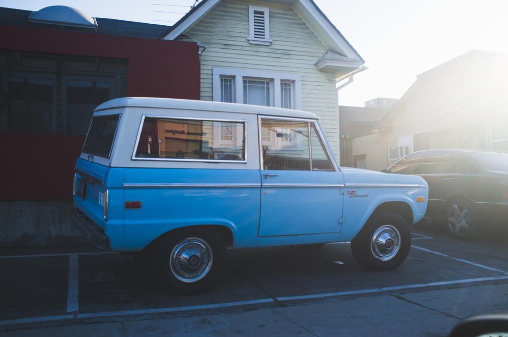Light blue vintage Ford Bronco with a white hardtop parked in a California parking space in warm afternoon light.