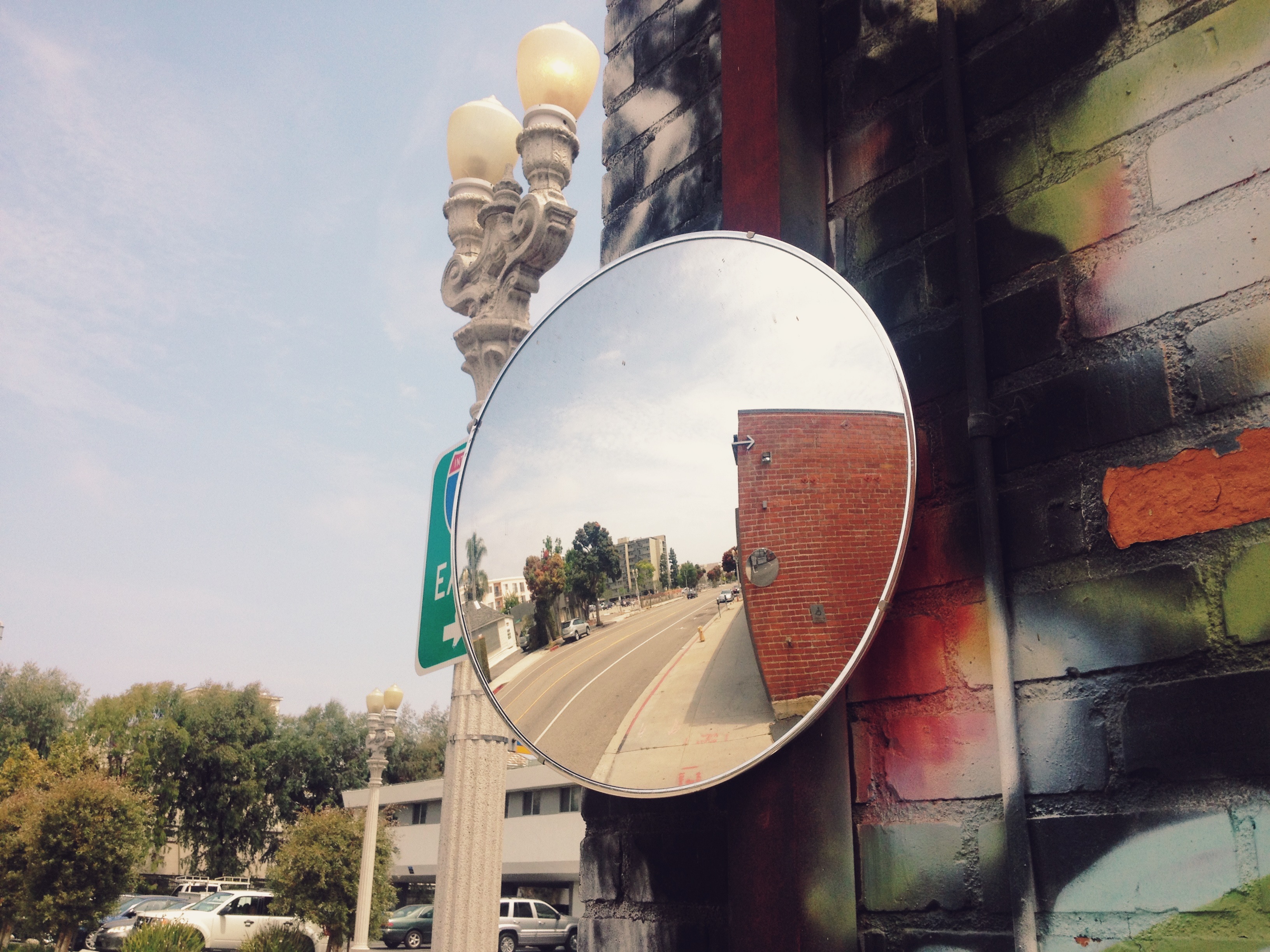 Convex traffic mirror on a spray-painted brick wall reflecting an empty California street.