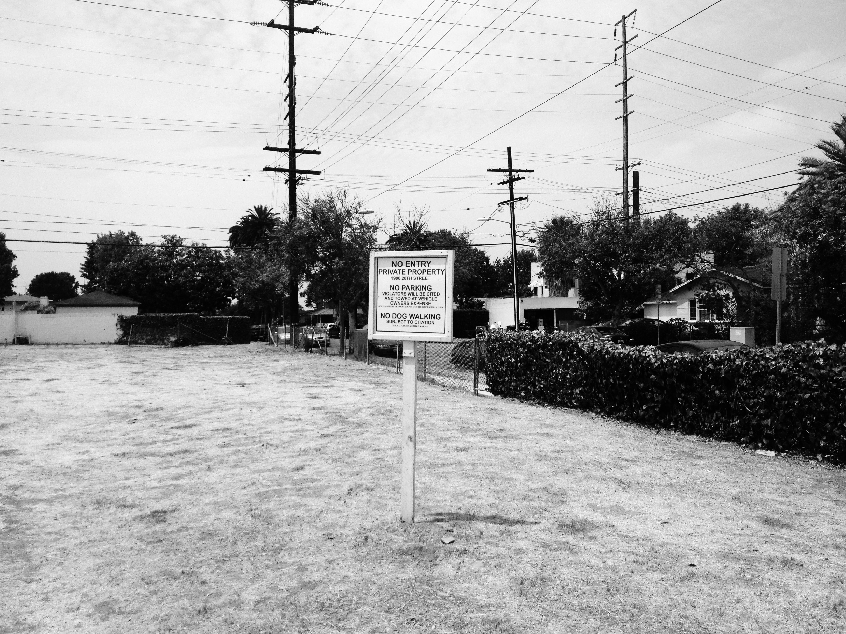 Dry grass lot with a 'NO ENTRY PRIVATE PROPERTY' sign under power lines, in black and white.