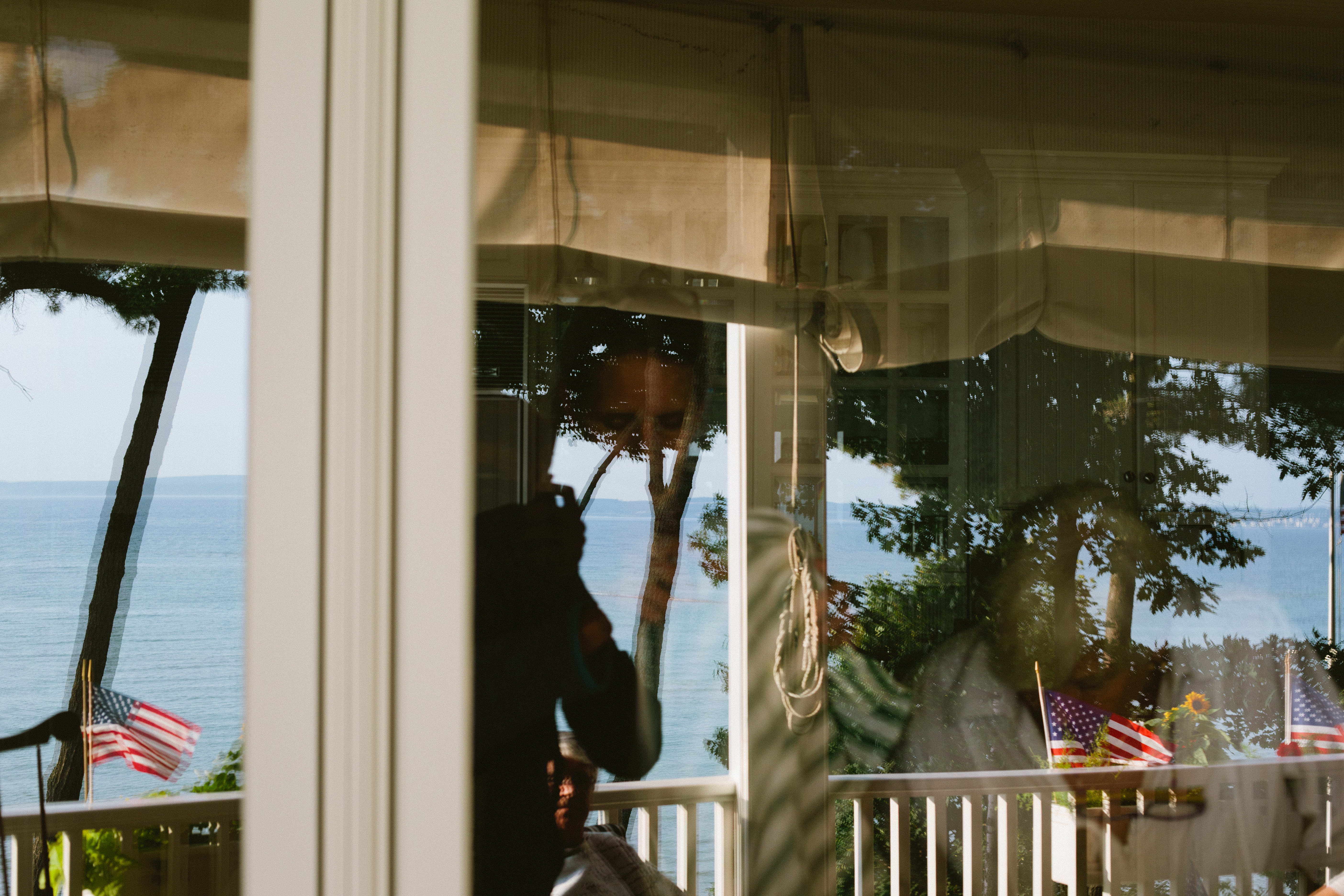 Window reflection framed by American flags on a wooden deck overlooking Lake Michigan in Harbor Springs.