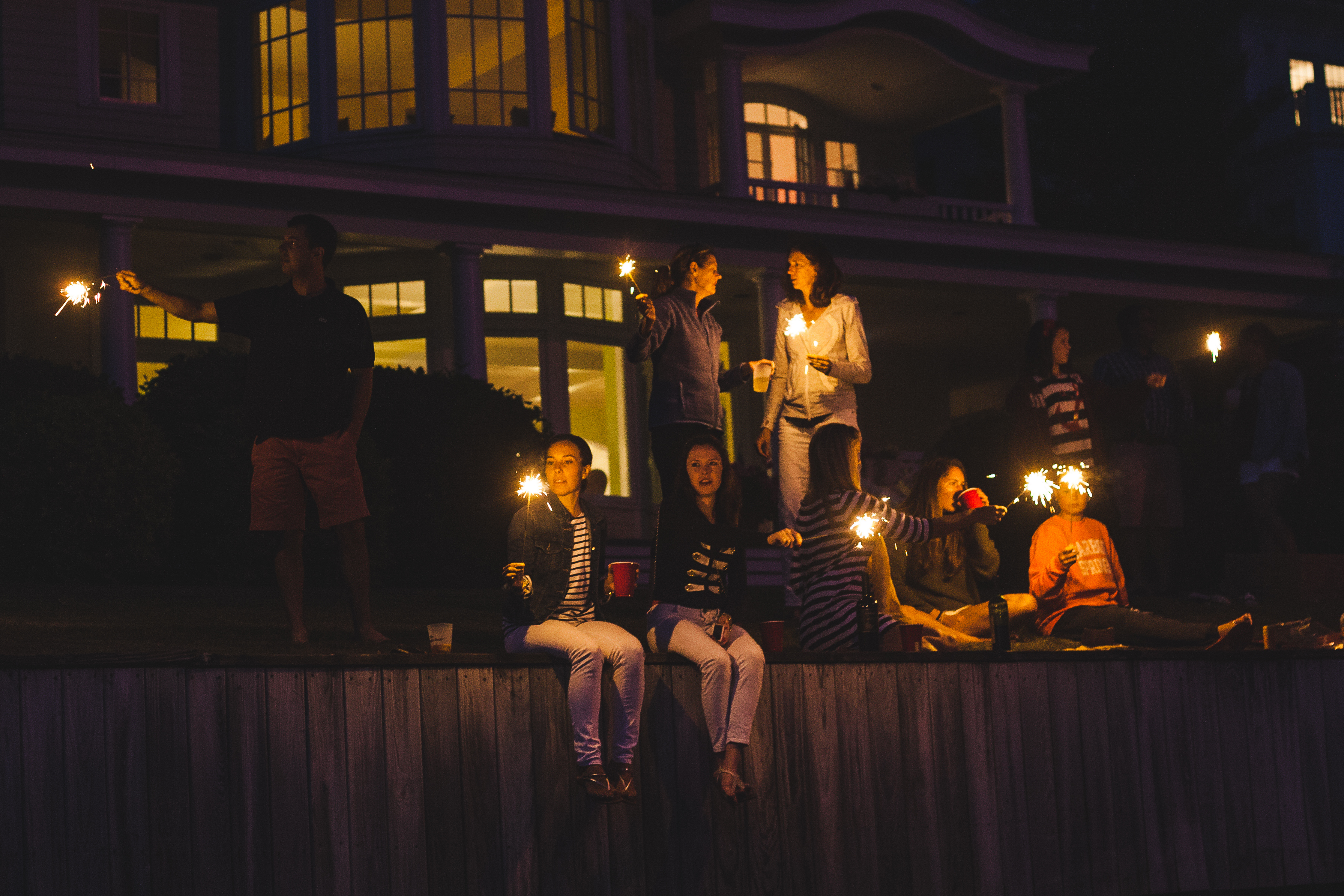 Gathering of friends and family waving sparklers at night in front of a shingle-style summer home in Harbor Springs, shot with a Canon 5D Mark II.