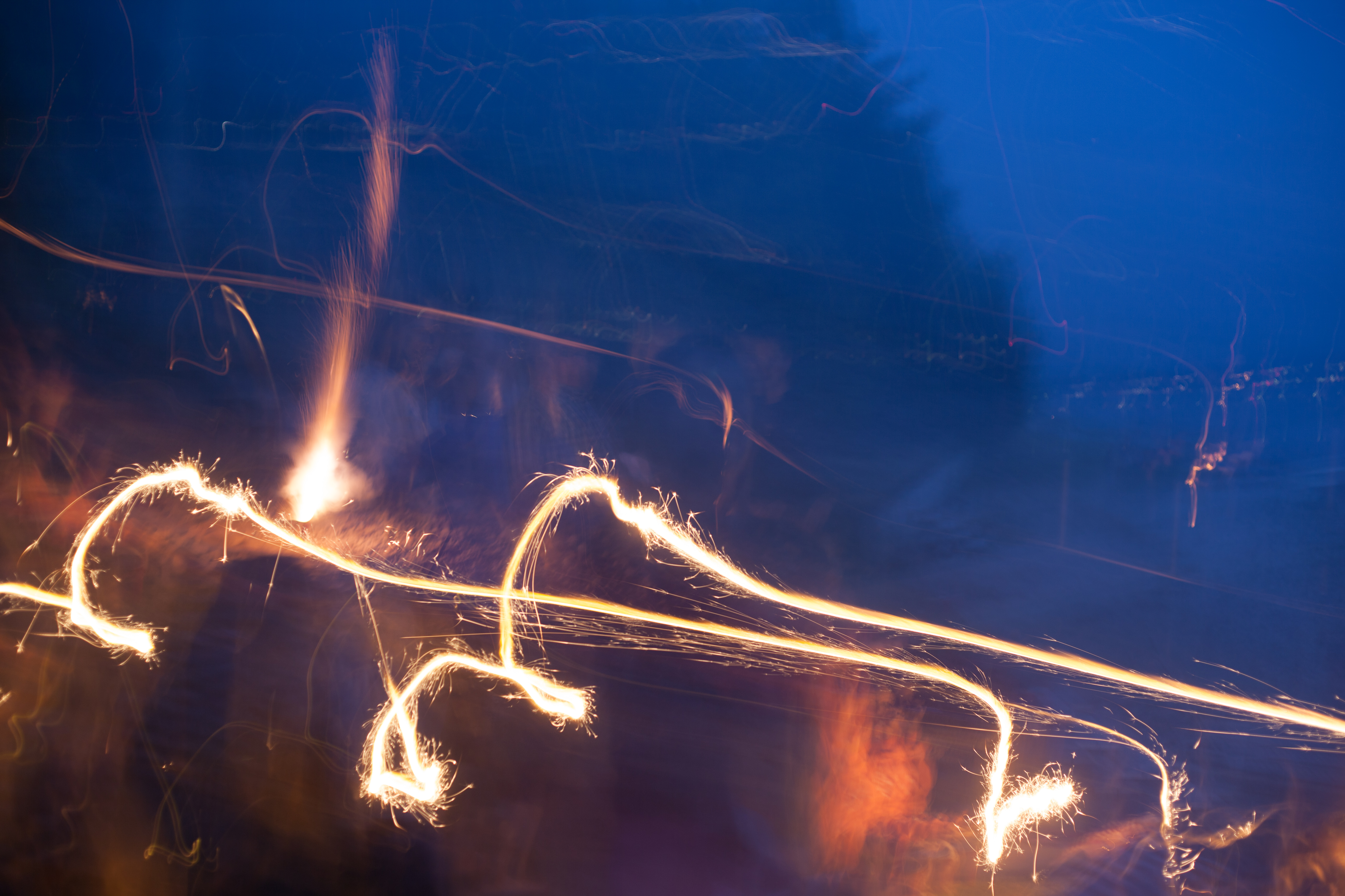 Abstract long-exposure light trails of burning sparklers dancing against a deep indigo night sky, shot with a Canon 5D Mark II.