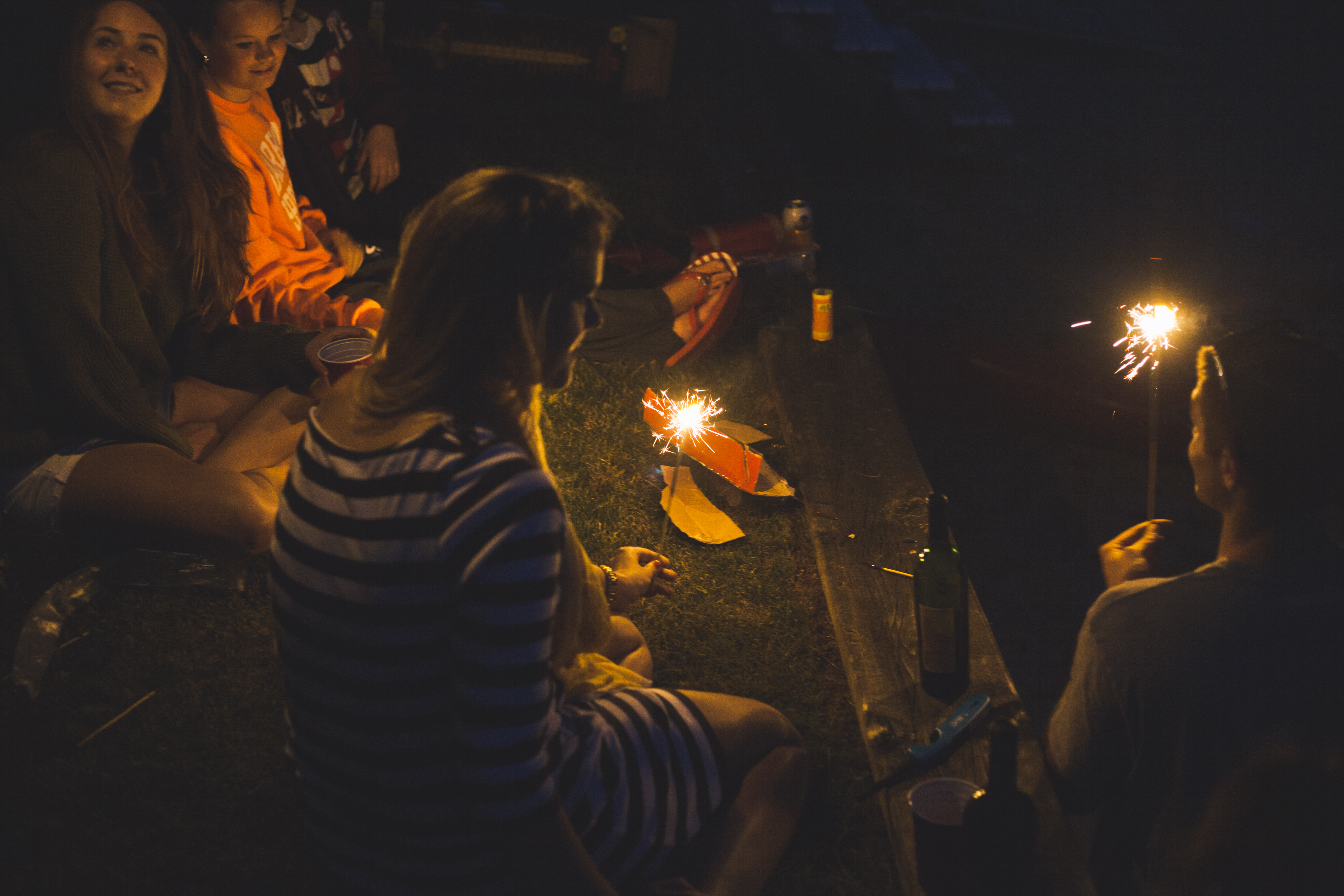 Over-the-shoulder candid view of friends gathered around glowing sparklers at night on the lawn, shot with a Canon 5D Mark II.