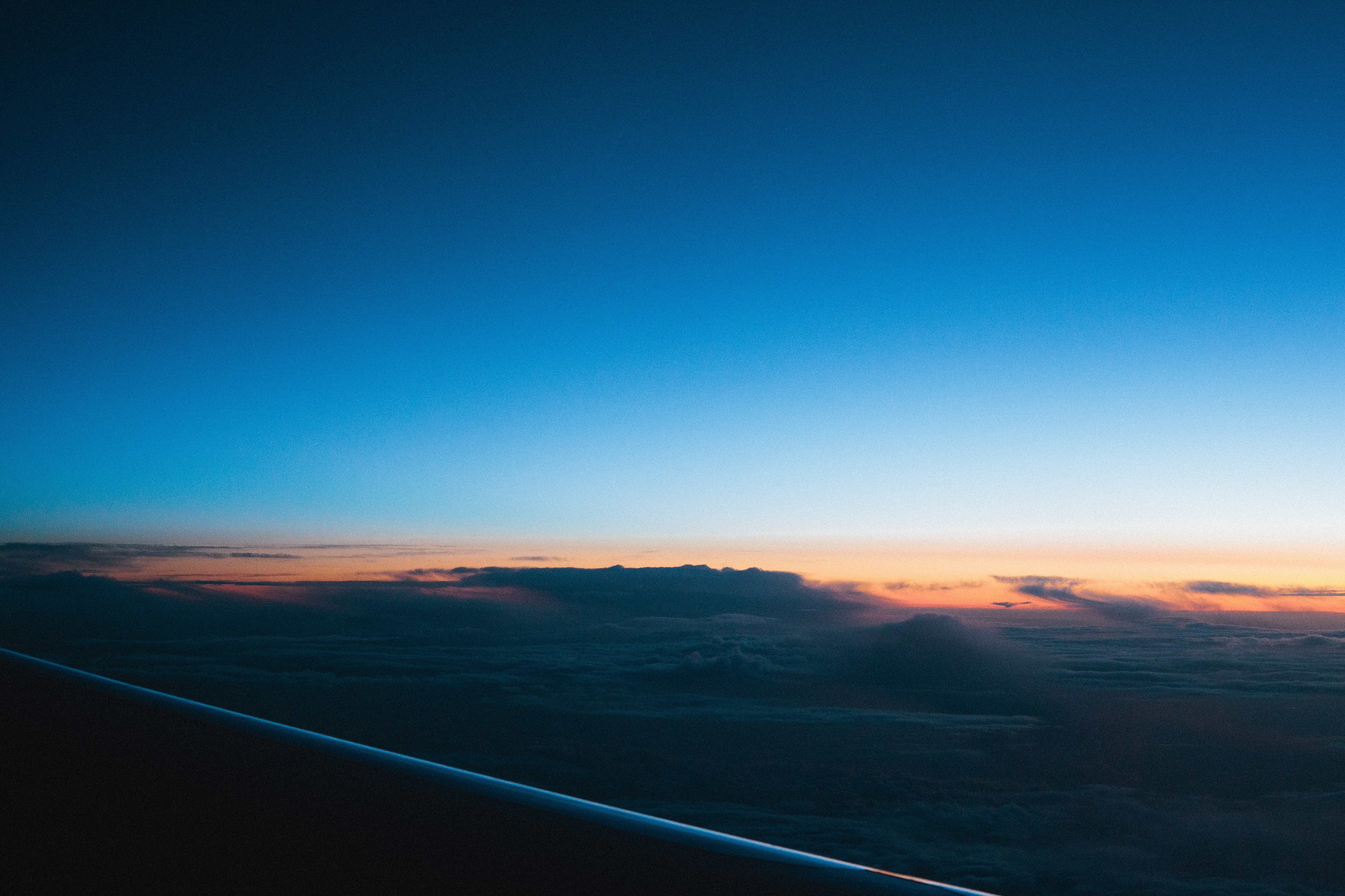 Golden sunset horizon and blue twilight above the clouds viewed through an airplane window.