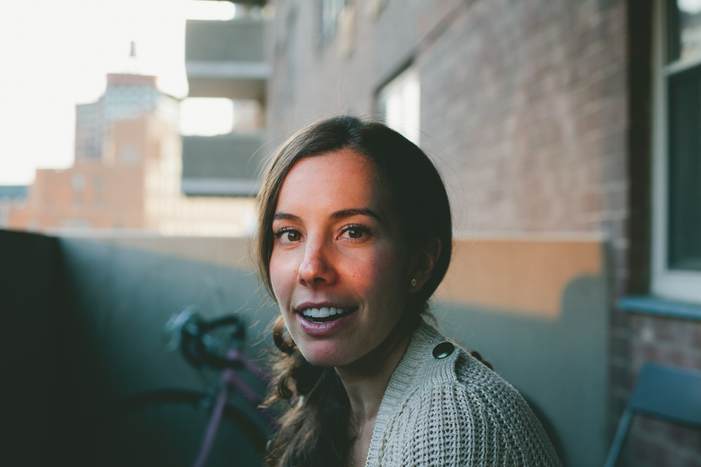 Meghan smiling on a city balcony at golden hour with an apartment building in the background.