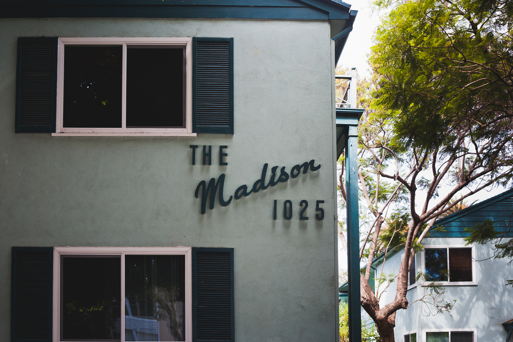 Pale green apartment building facade with dark window shutters and vintage signage reading 'THE Madison 1025'.