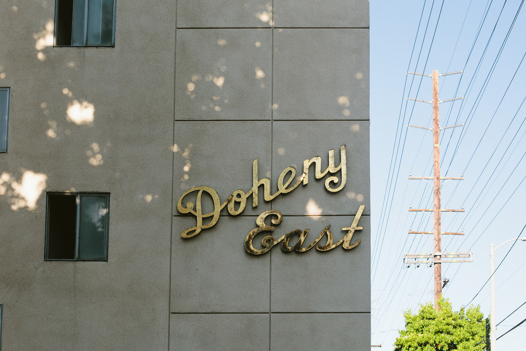 Sign reading 'Doheny East' in golden script on the concrete facade of an apartment building.