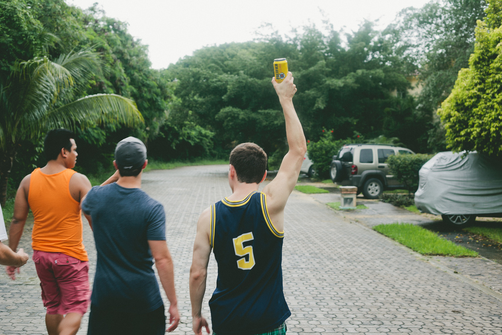 Three young men walking down a tropical street, one holding a yellow can of Pacifico beer.