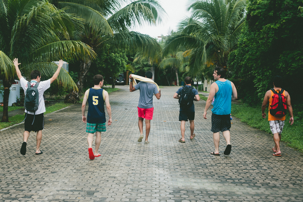 Six friends walking down a cobblestone road lined with tall palm trees in Playa del Carmen.