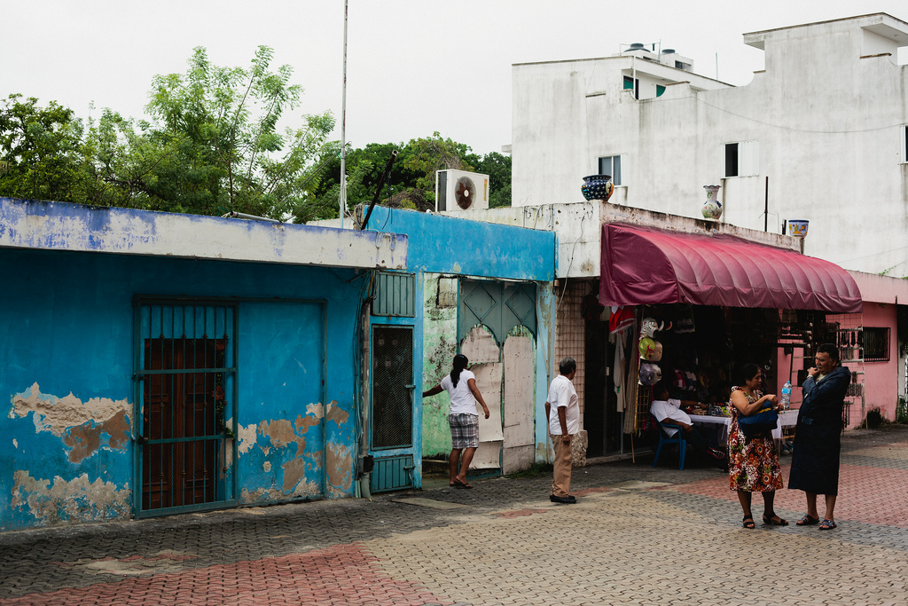 Bright cyan and pink buildings along a paved plaza with pedestrians in Playa del Carmen.