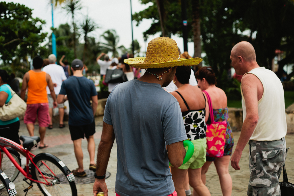 Man in a yellow straw hat walking through a crowded plaza in Playa del Carmen with a red bicycle.