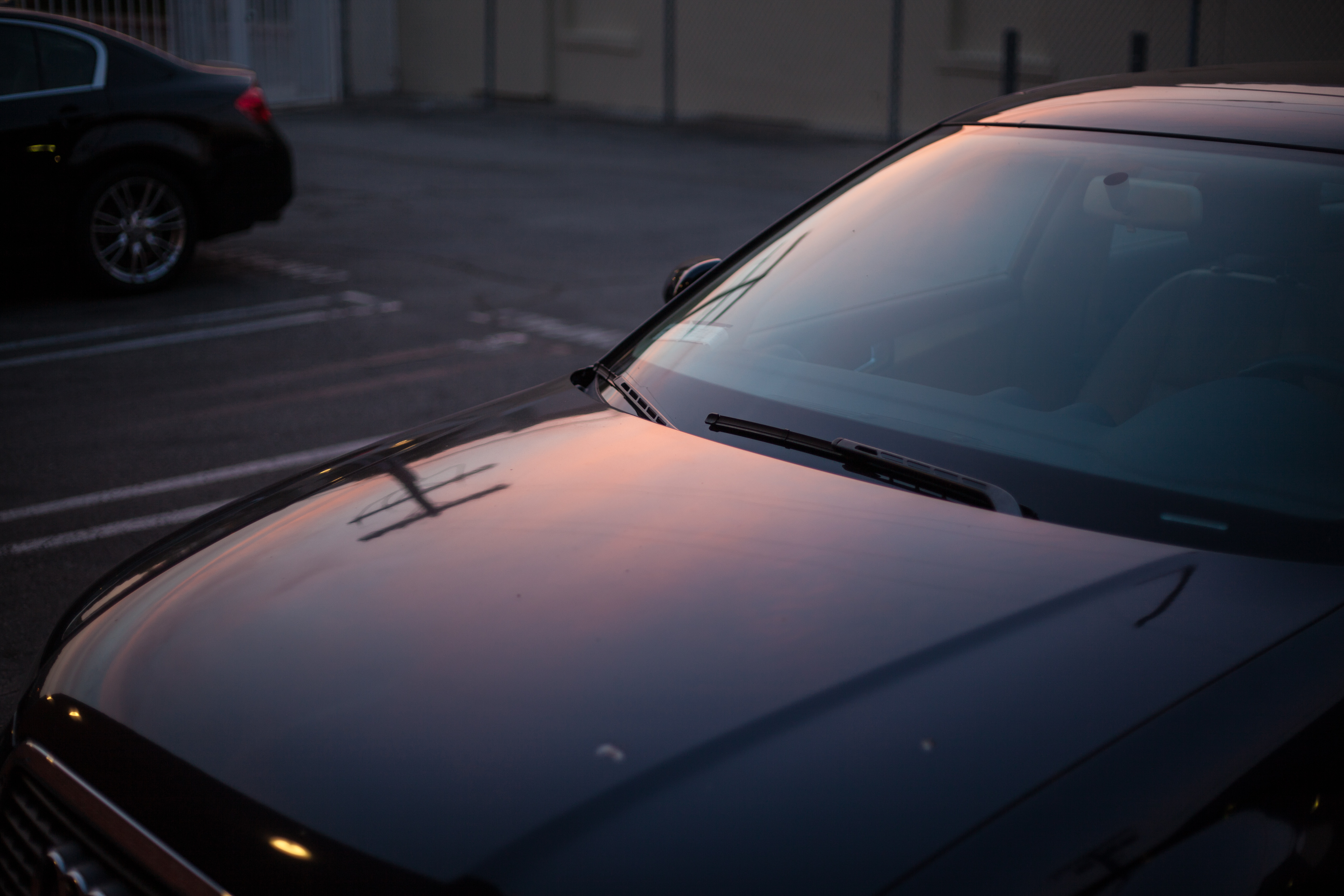 Glossy hood of a dark car reflecting the soft warm hues of an evening sunset and telephone wires in a parking lot.