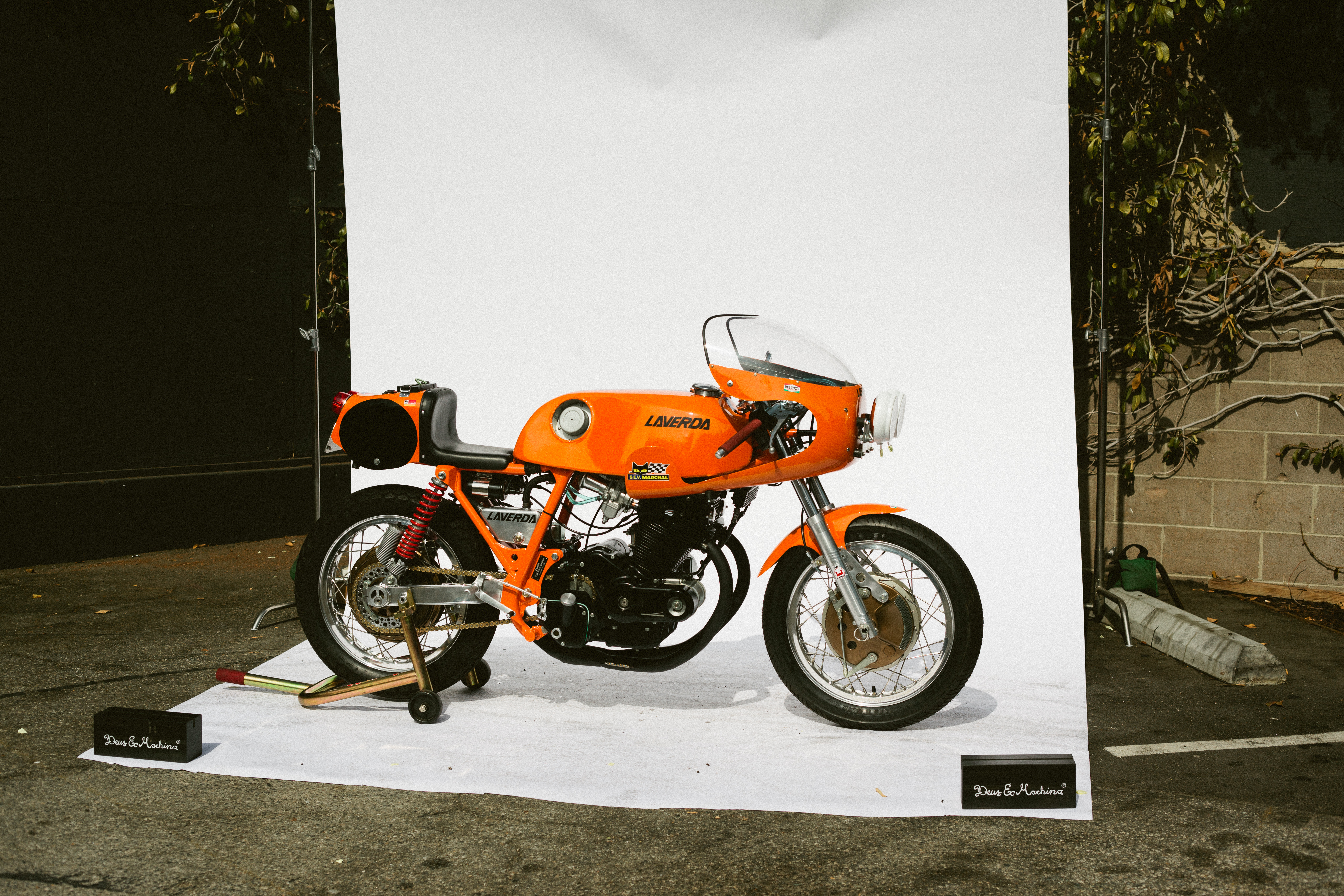 Bright orange vintage Laverda road racer motorcycle displayed on a white backdrop at Deus Bike Build Off.