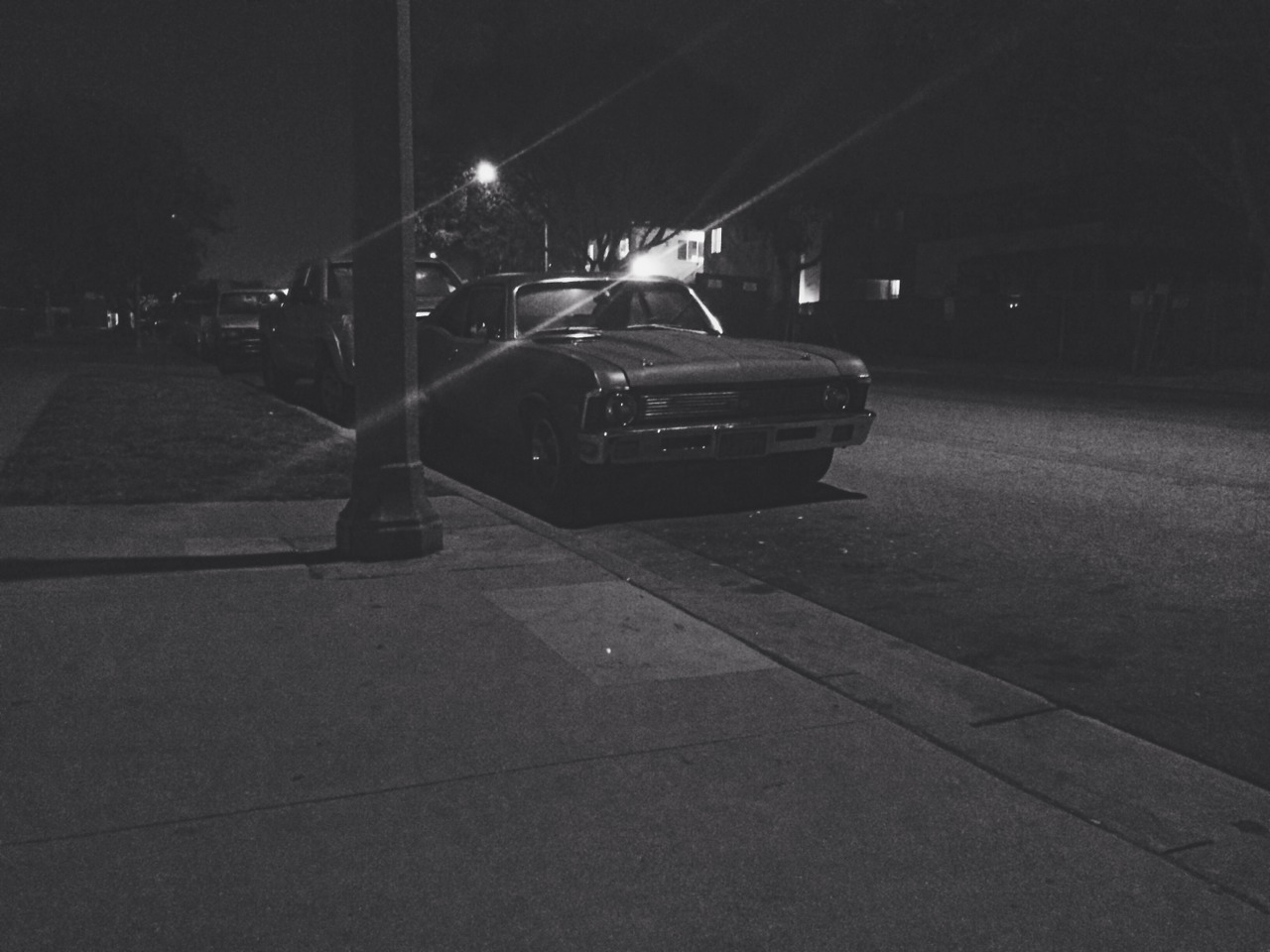 Classic Chevrolet parked along a residential curb at night under a streetlight, in black and white.