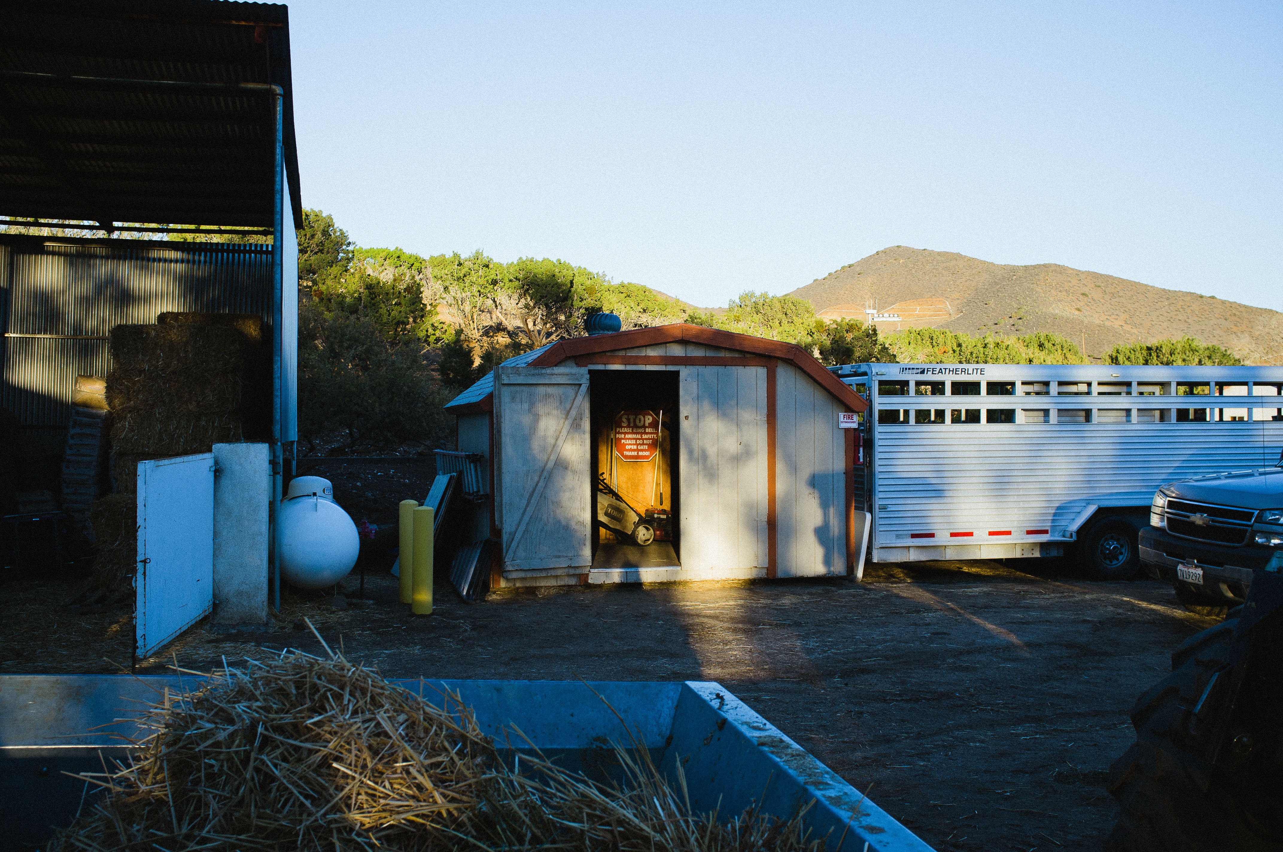 Wooden shed with an animal safety sign beside a Featherlite trailer and barn at Farm Sanctuary.