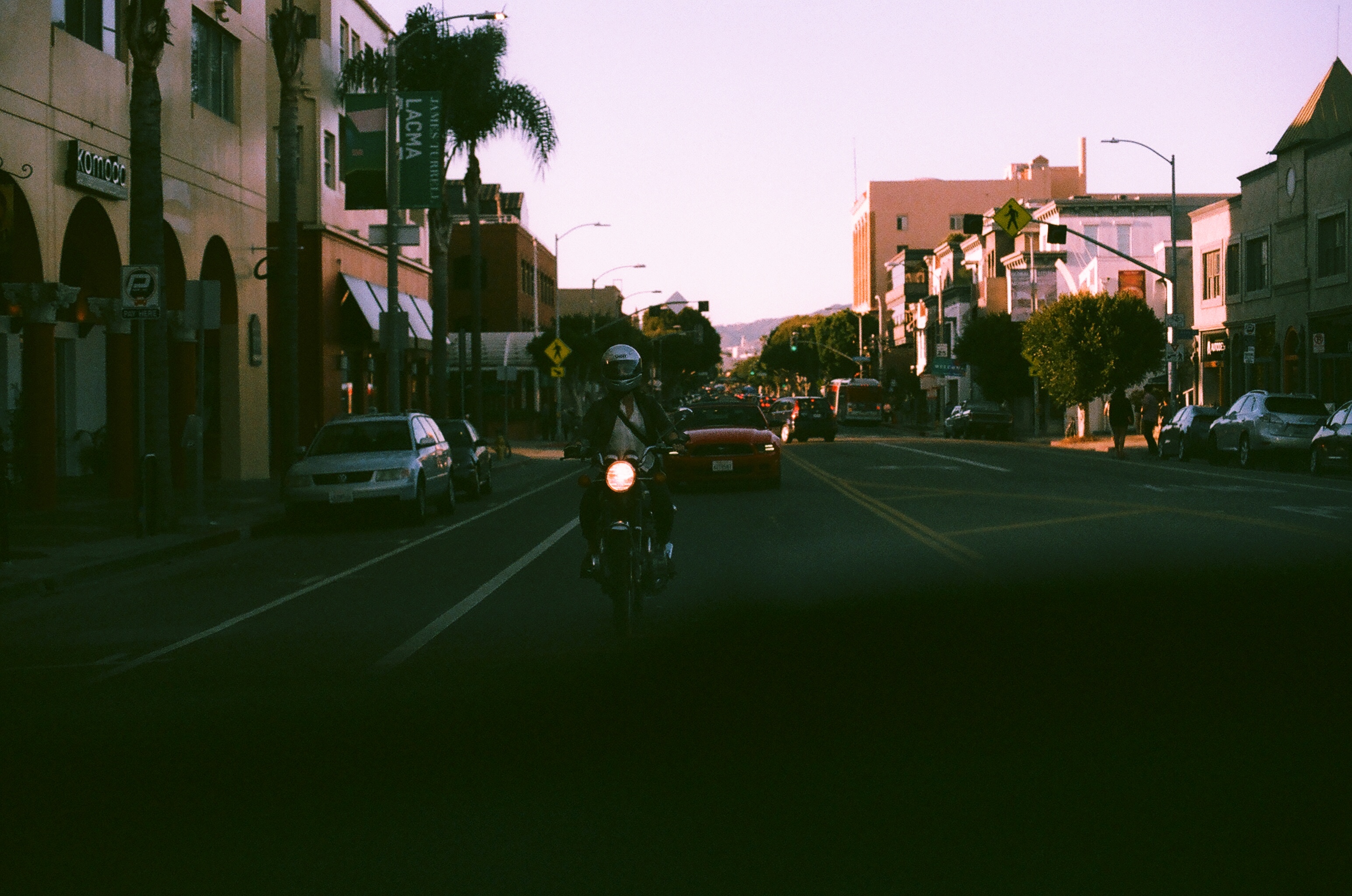 Motorcyclist riding down an avenue flanked by shops and palm trees at dusk in Venice, California.