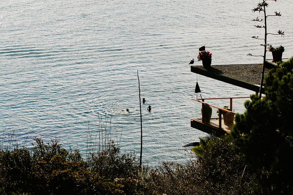 Architectural balcony perched above the ocean with people swimming in coastal waters below.