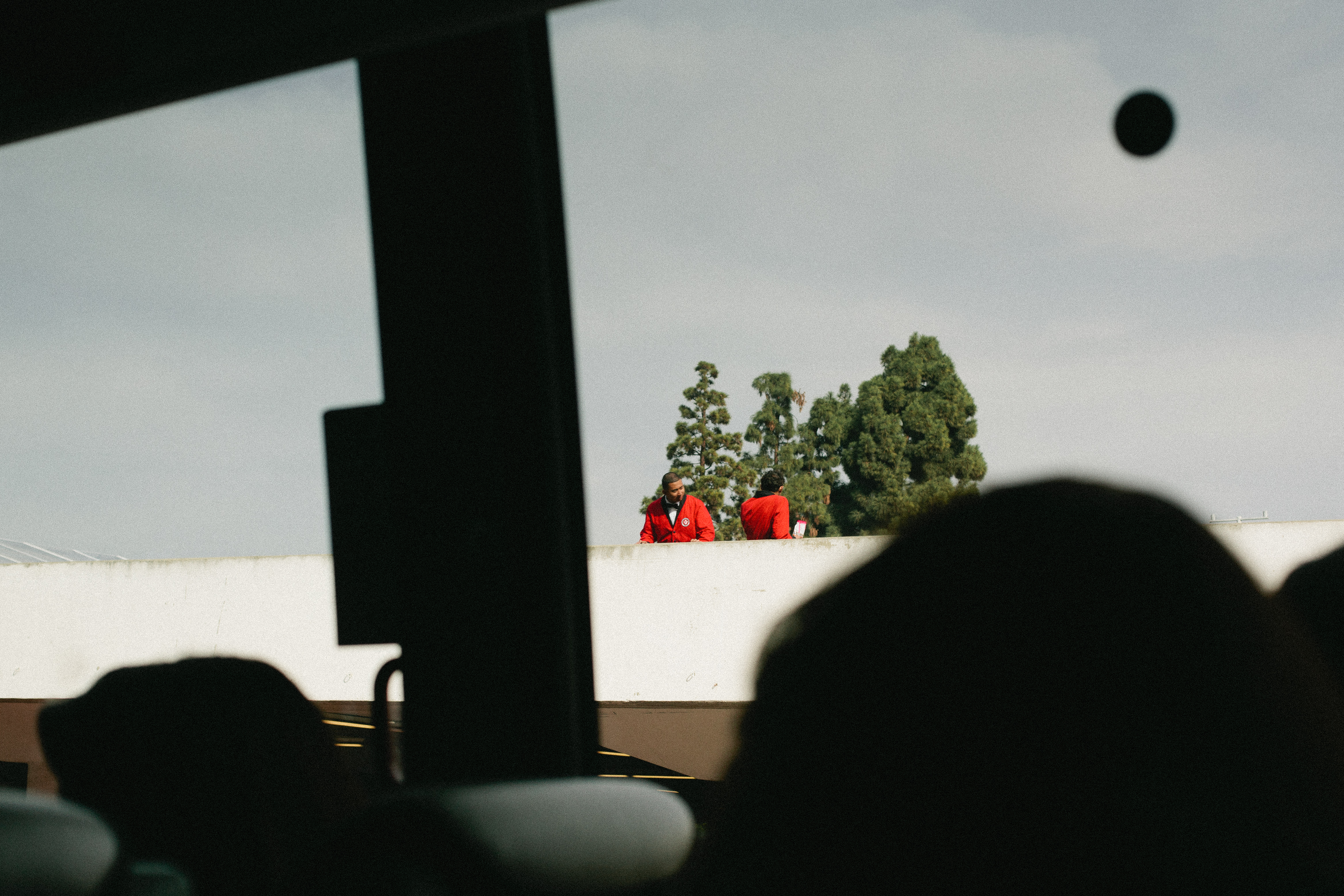Security personnel in red blazers standing atop a white wall near pine trees at the Golden Globe Awards.