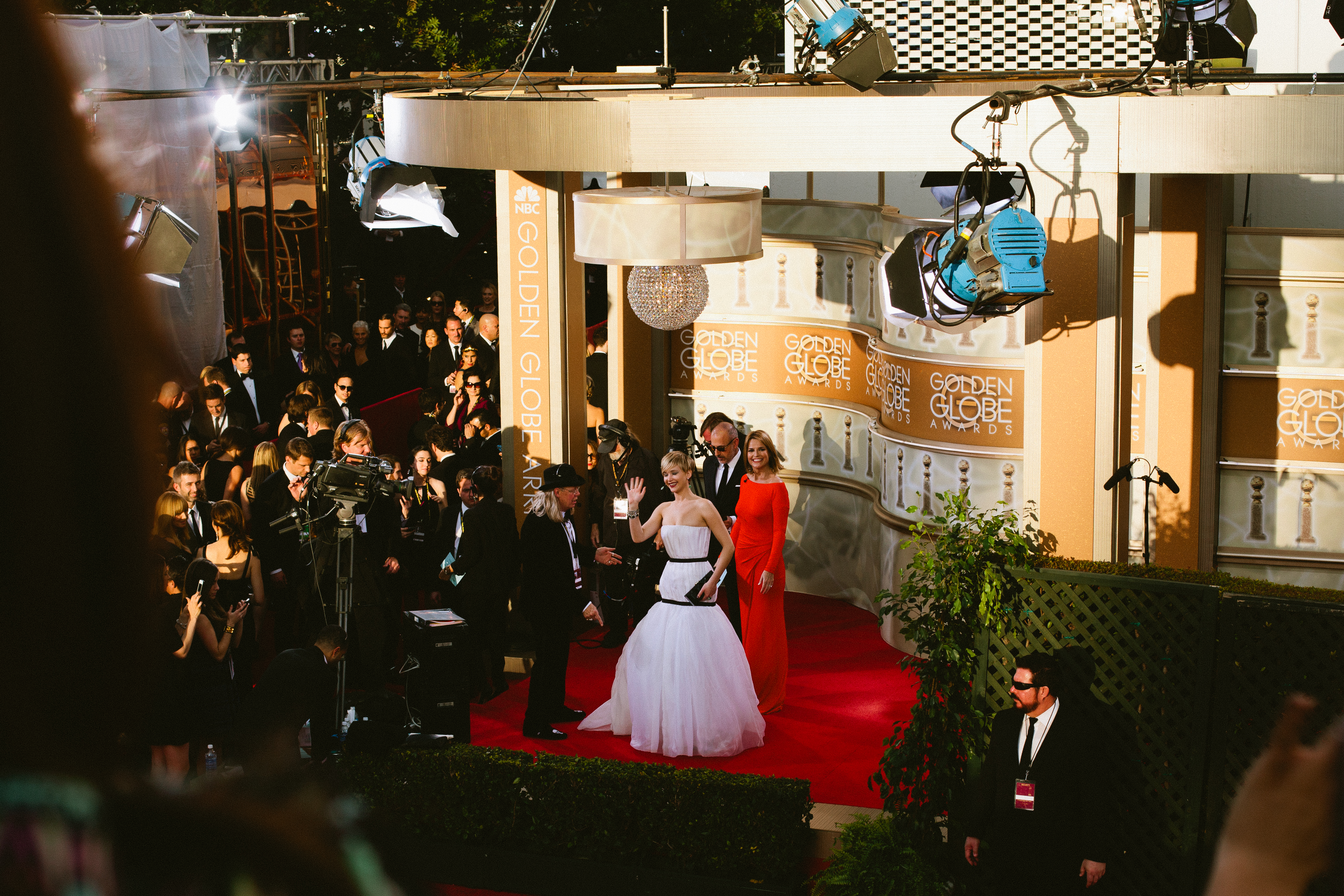 Jennifer Lawrence in a white Dior gown waving from the red carpet interview stage at the Golden Globes.