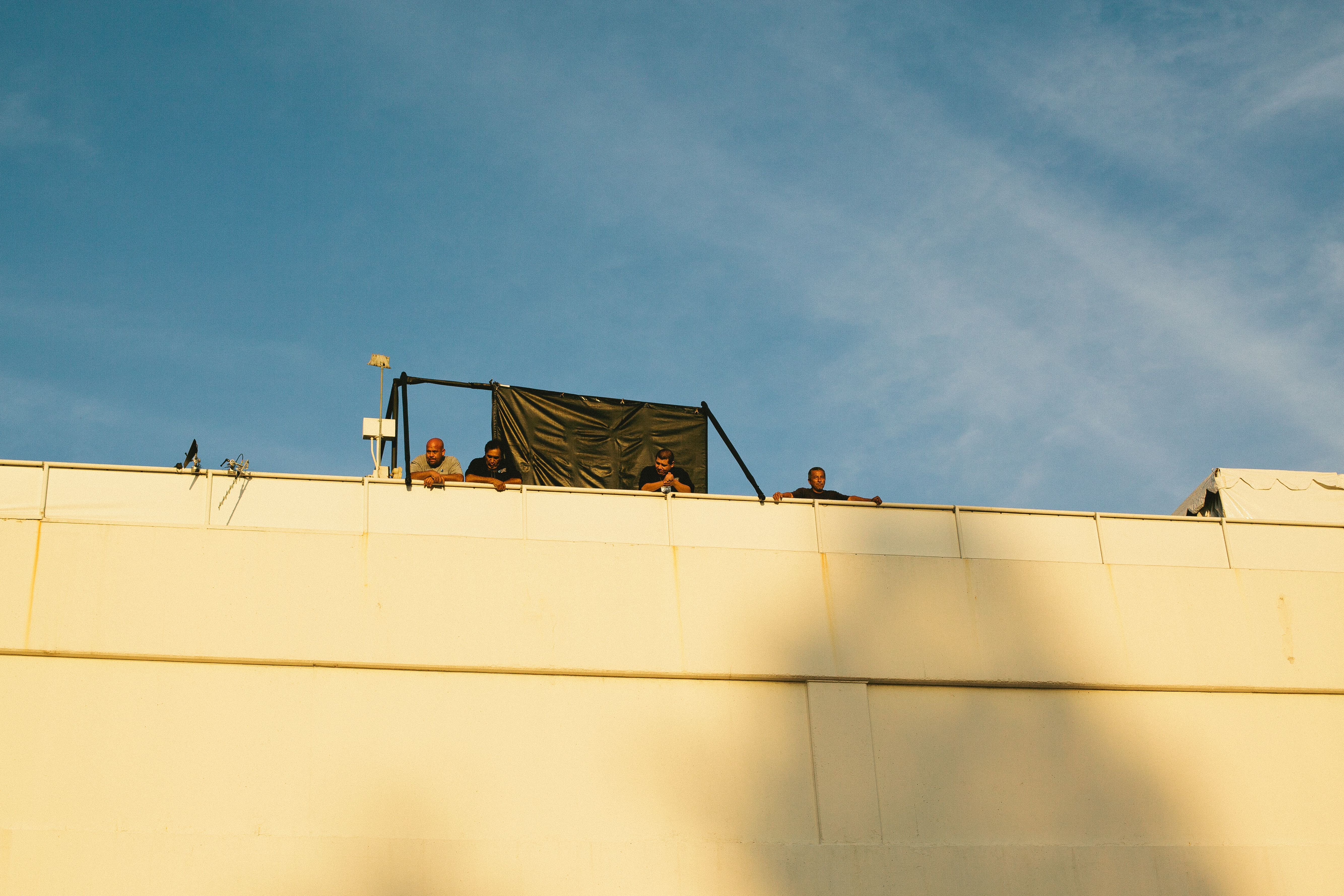 Crew members leaning over a white retaining wall watching Golden Globe Awards preparations below.