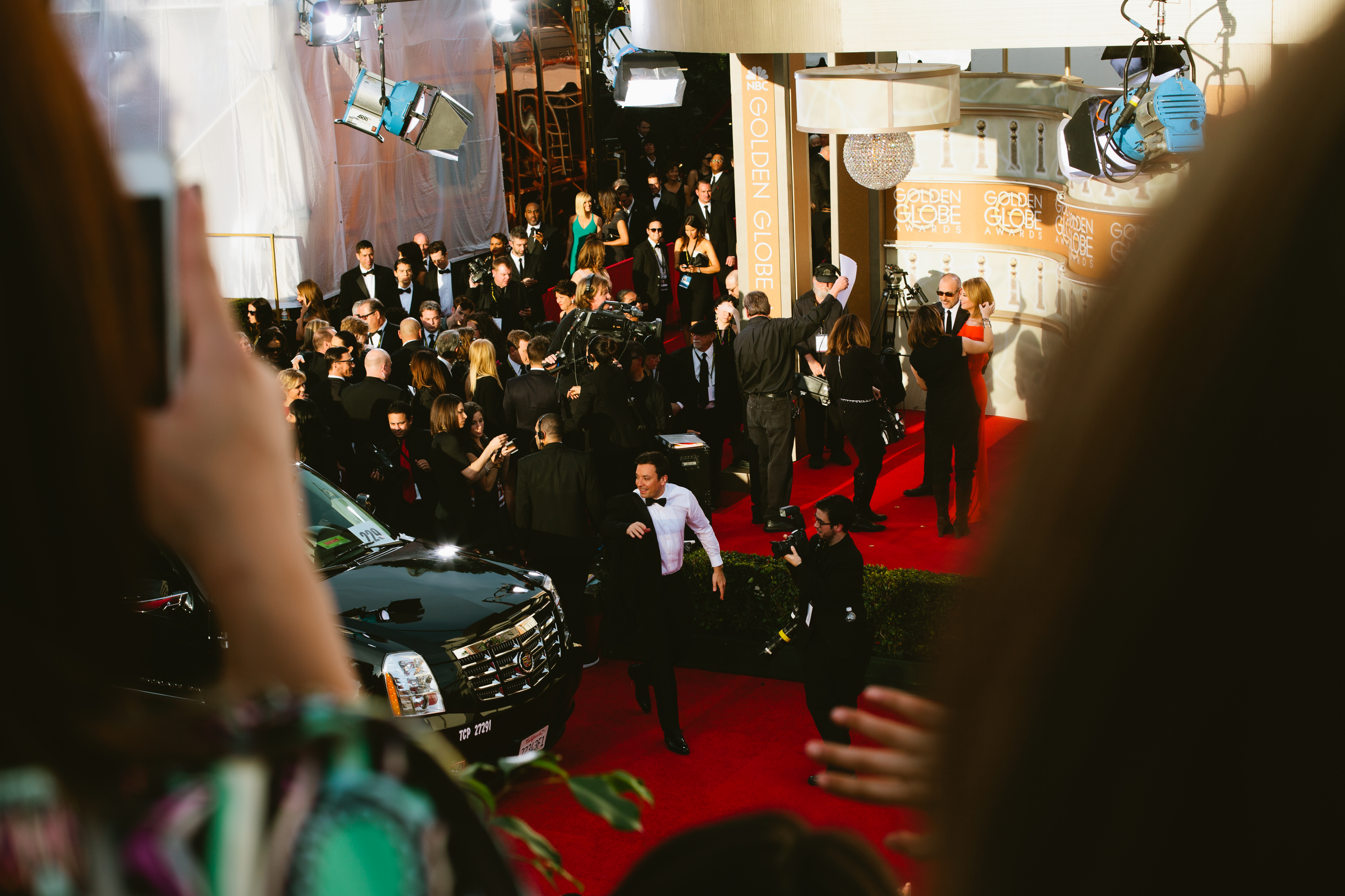 Jimmy Fallon jogging across the Golden Globe Awards red carpet beside a black SUV and crowds.