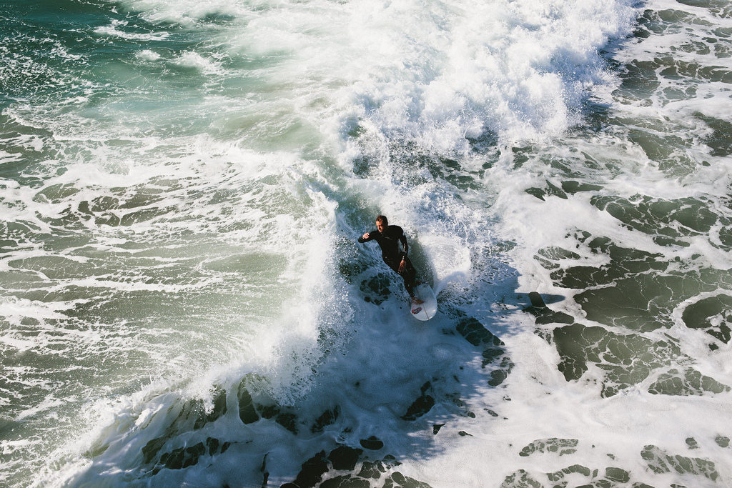 High-angle view of a surfer in a black wetsuit carving through swirling white foamy wave break, shot with a Canon 5D Mark II.