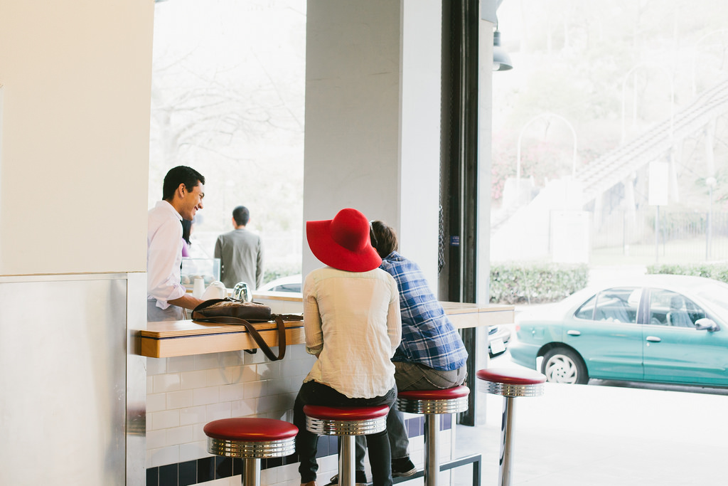 Customers seated at a retro lunch counter on red swivel stools talking with a barista in Los Angeles.