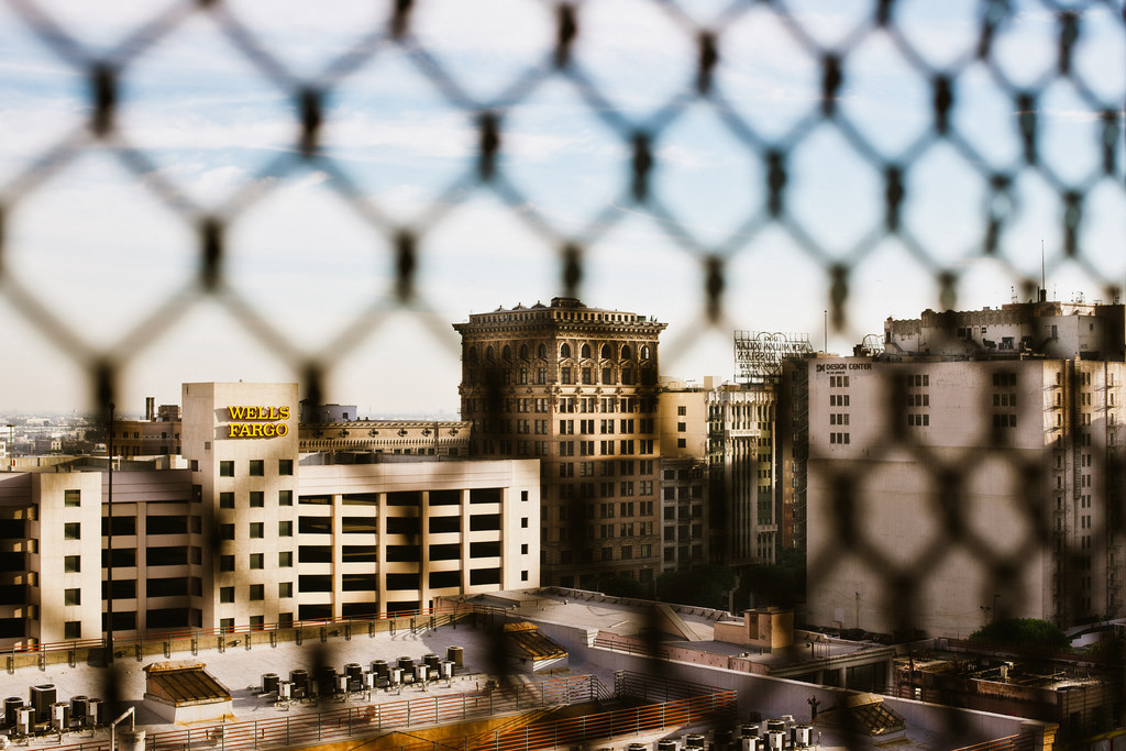 Downtown Los Angeles buildings including a Wells Fargo facility seen through a chain-link fence.