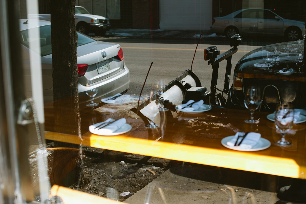 Window reflection combining a table set with wine glasses and an outdoor Chicago street in winter.