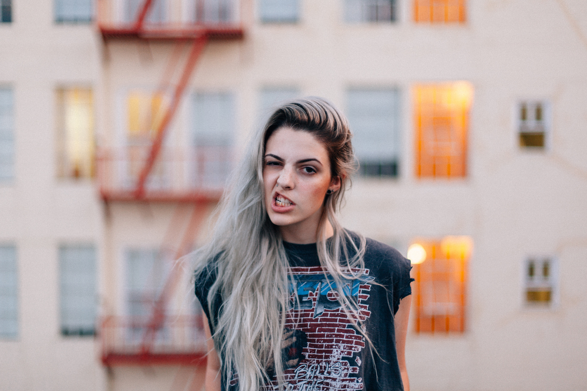 Shelby Parks with blonde hair and a nose stud making a playfully defiant expression outside an apartment.