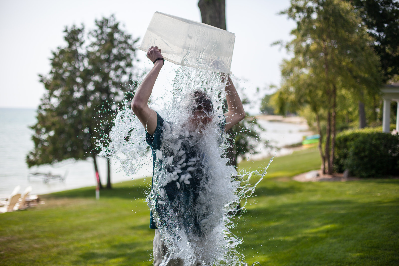 Man dumping a bin of ice water over his head for the ALS Ice Bucket Challenge on a lawn by a lake.