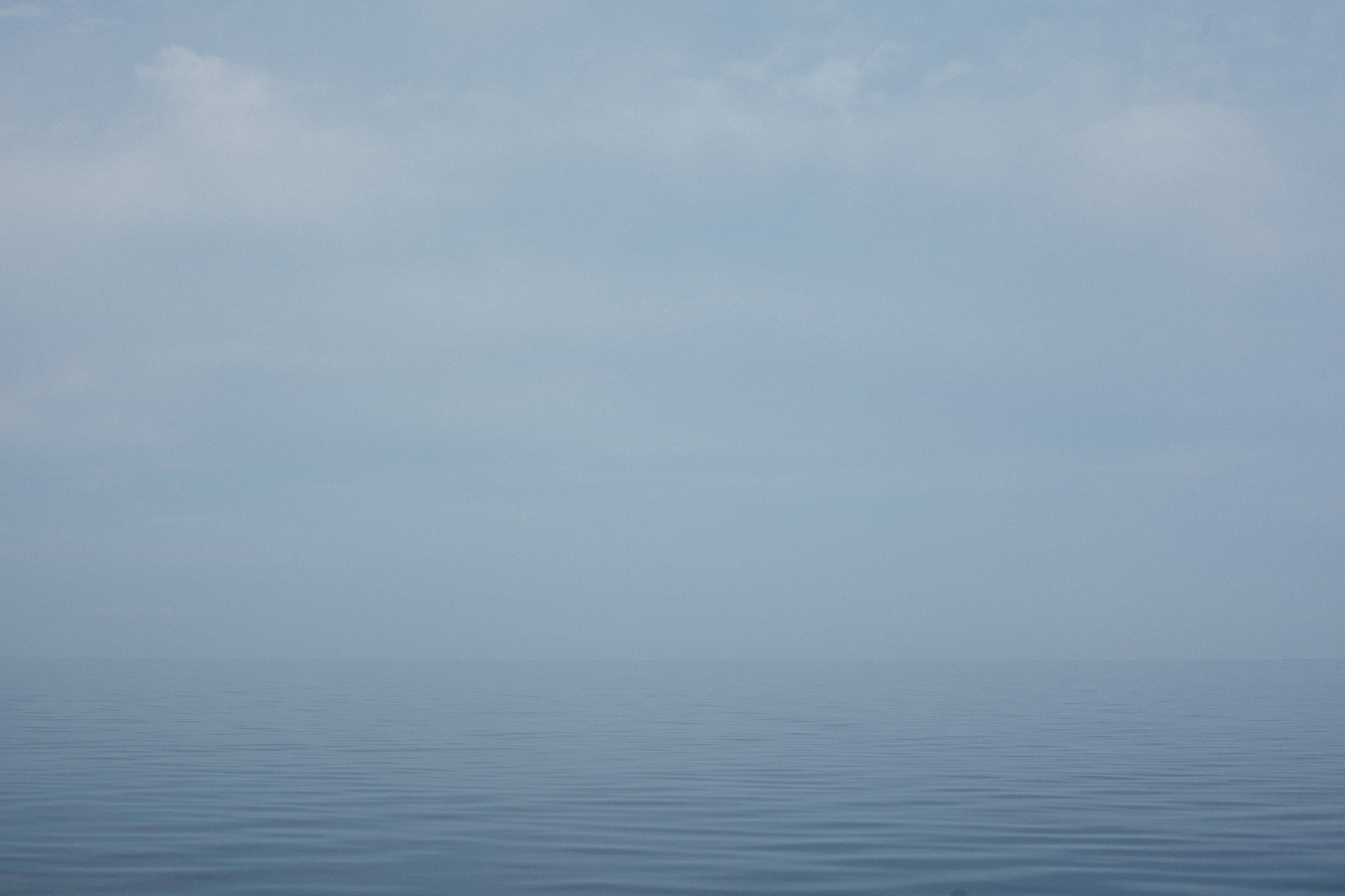 Serene minimalist seascape of calm, flat blue water dissolving into a pale hazy horizon on Lake Michigan.