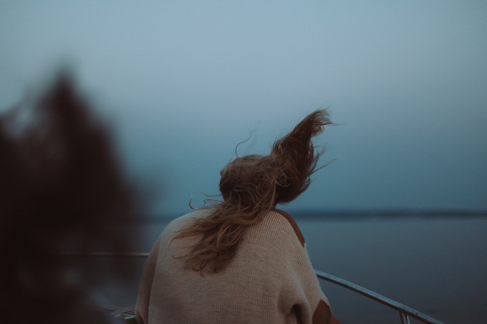 Woman in a chunky knit sweater on a boat with her hair lifted dramatically by the wind over open water.
