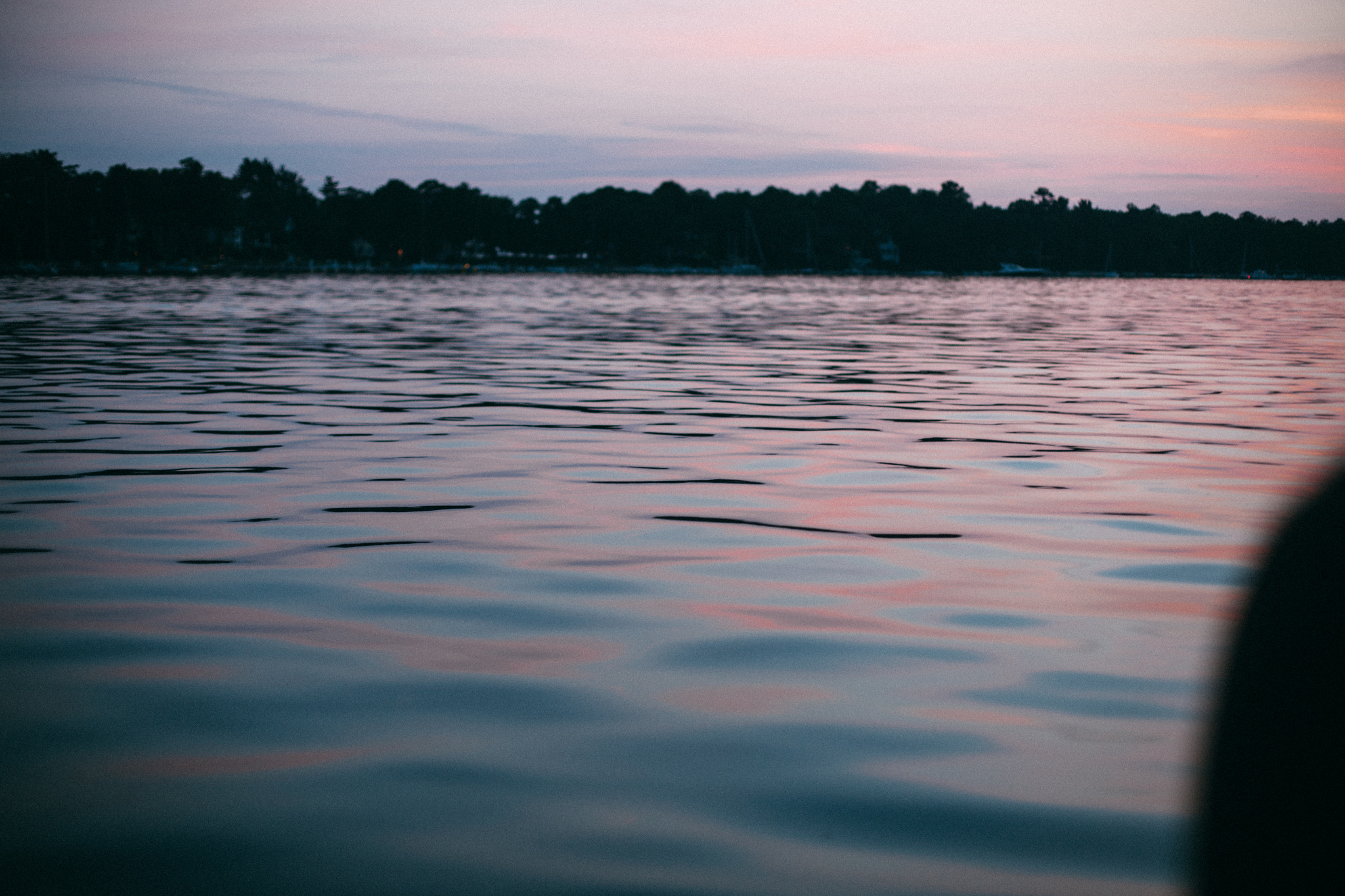 Low-angle view across gentle rippling lake water reflecting the soft pink and violet hues of a summer sunset.