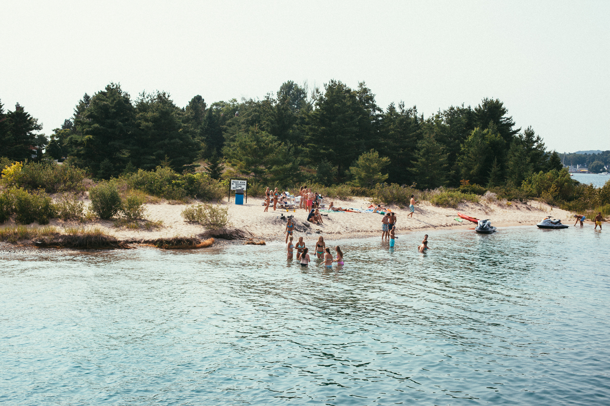 Summer swimmers and sunbathers enjoying a sunny sandy cove bordered by evergreen pine trees along the shoreline of Lake Michigan, shot with a Canon 5D Mark II.