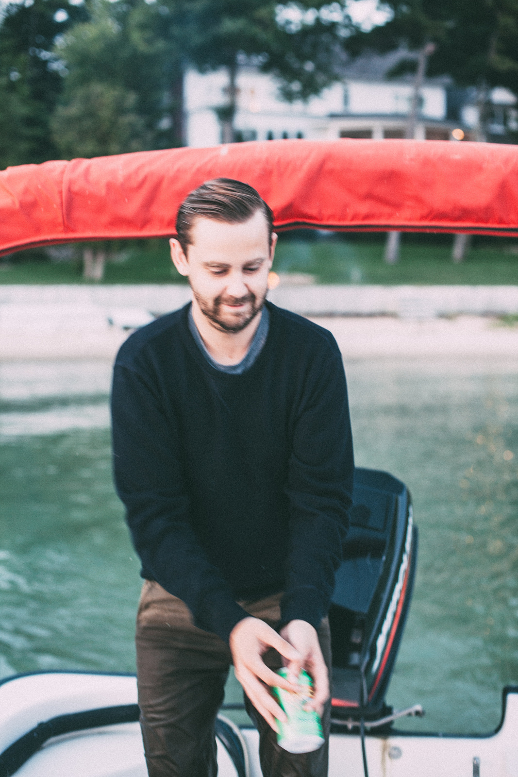Candid portrait of a smiling man in a dark crewneck sweater on a boat beneath a red canopy holding a drink on Lake Michigan, shot with a Canon 5D Mark II.