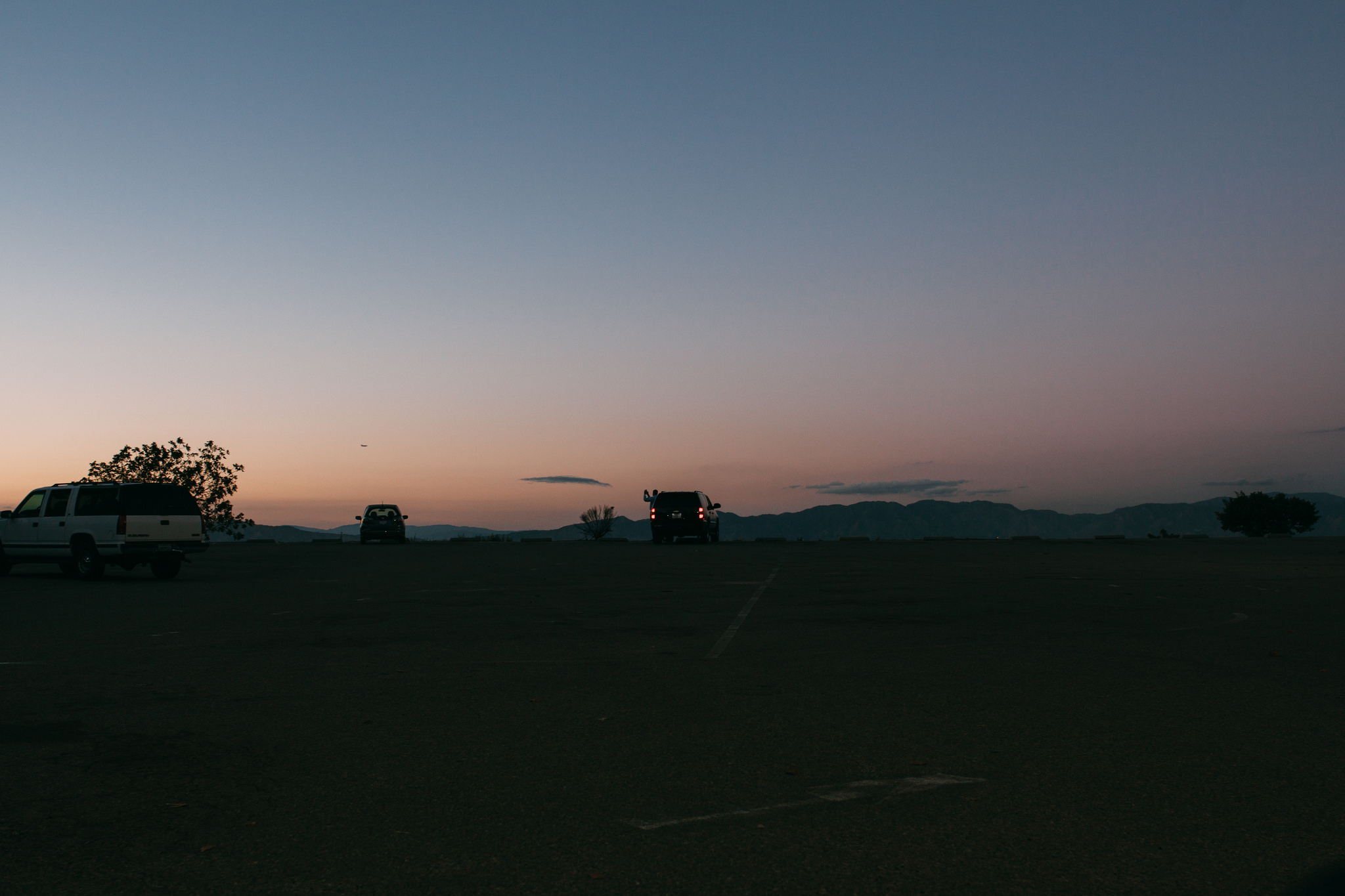 Asphalt parking overlook at dusk with parked SUVs against distant mountain ridges under an evening sky.