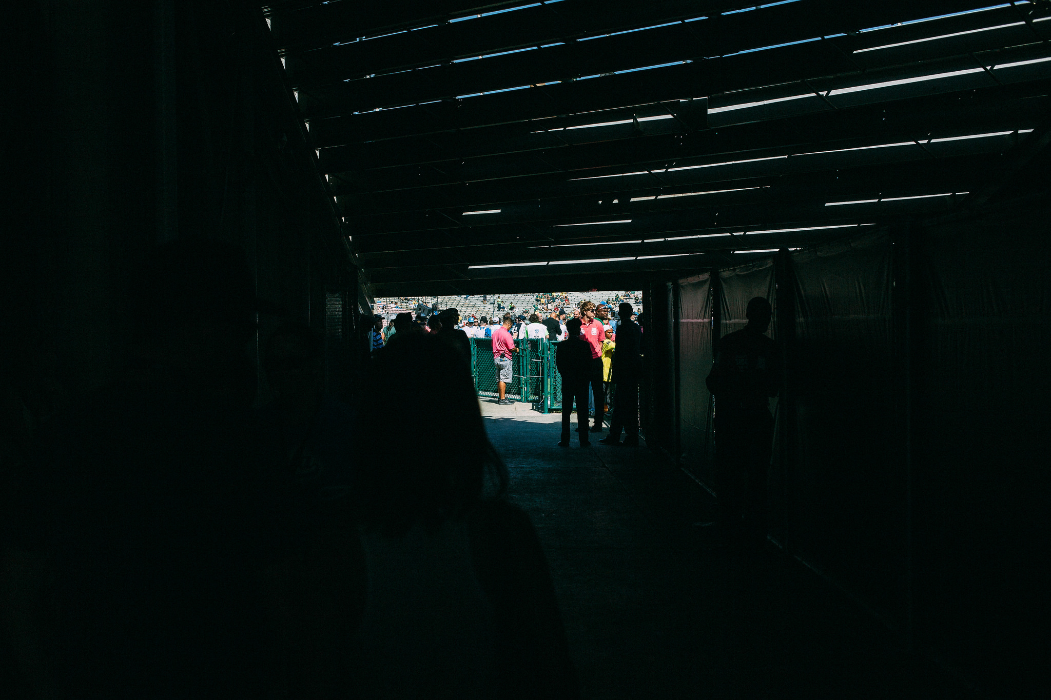 View from the dark concourse tunnel toward the sunlit Rose Bowl seating area with staff by the gate.