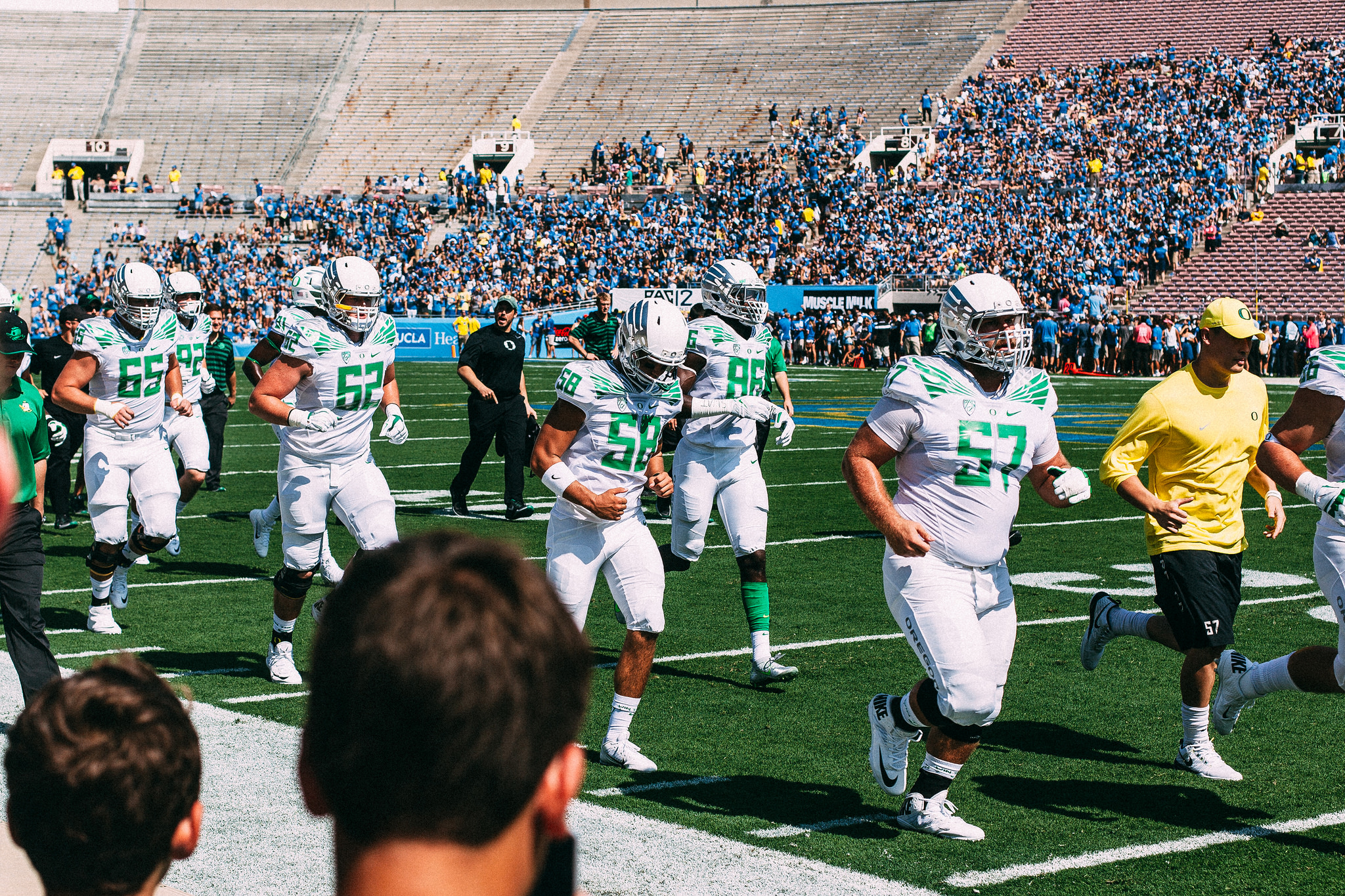 Oregon Ducks football players in white and green jogging onto the field at a packed Rose Bowl stadium.