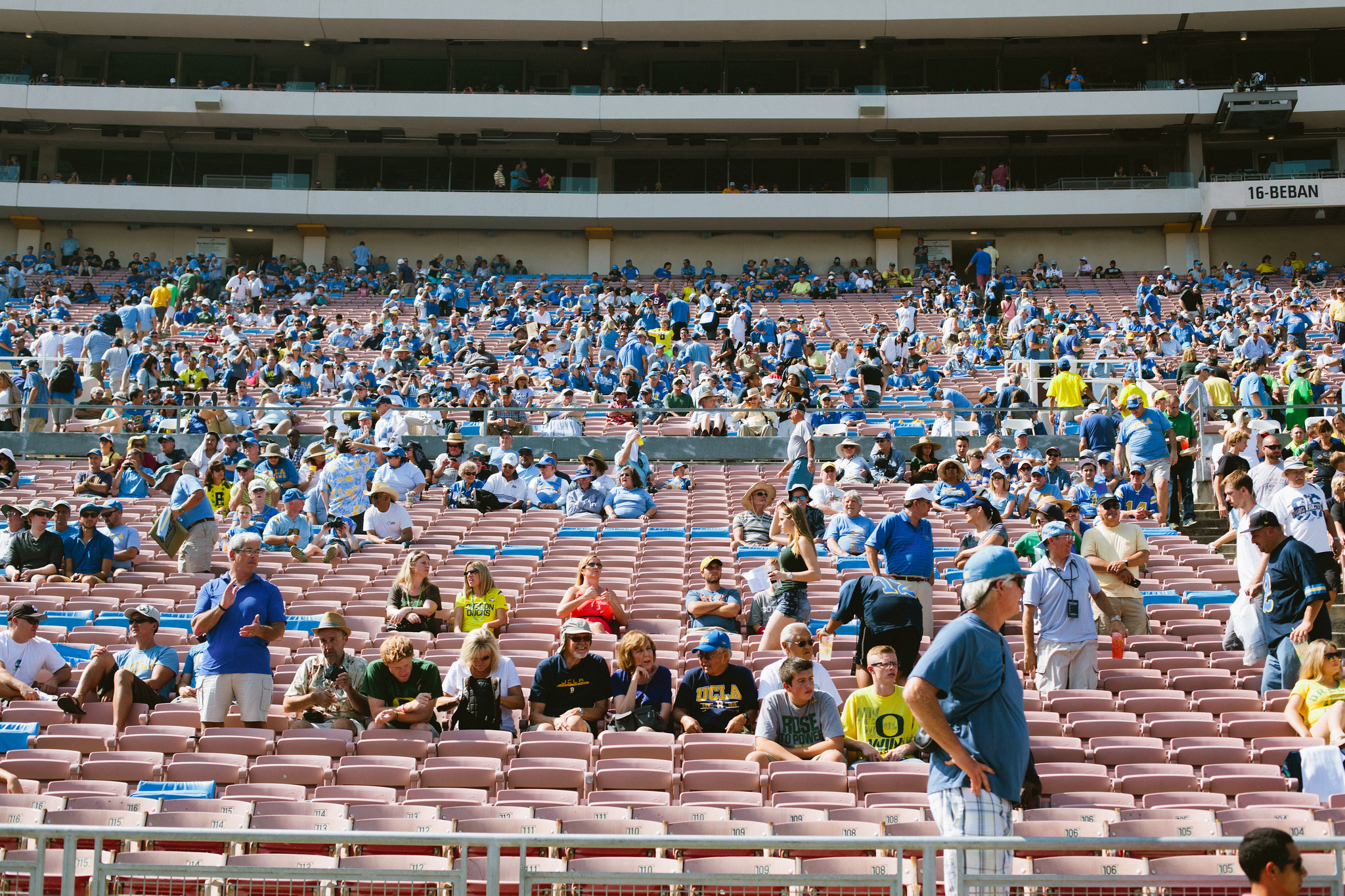 Spectators in blue and gold seated in the Rose Bowl grandstands during a sunny daytime football game.