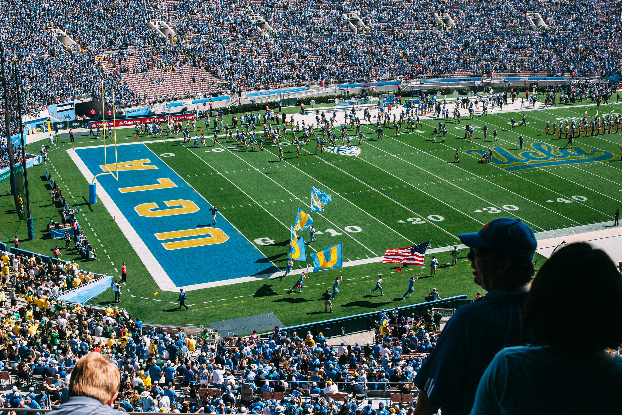 Rose Bowl end zone with UCLA lettering as cheerleaders carry flags and the team enters the field.