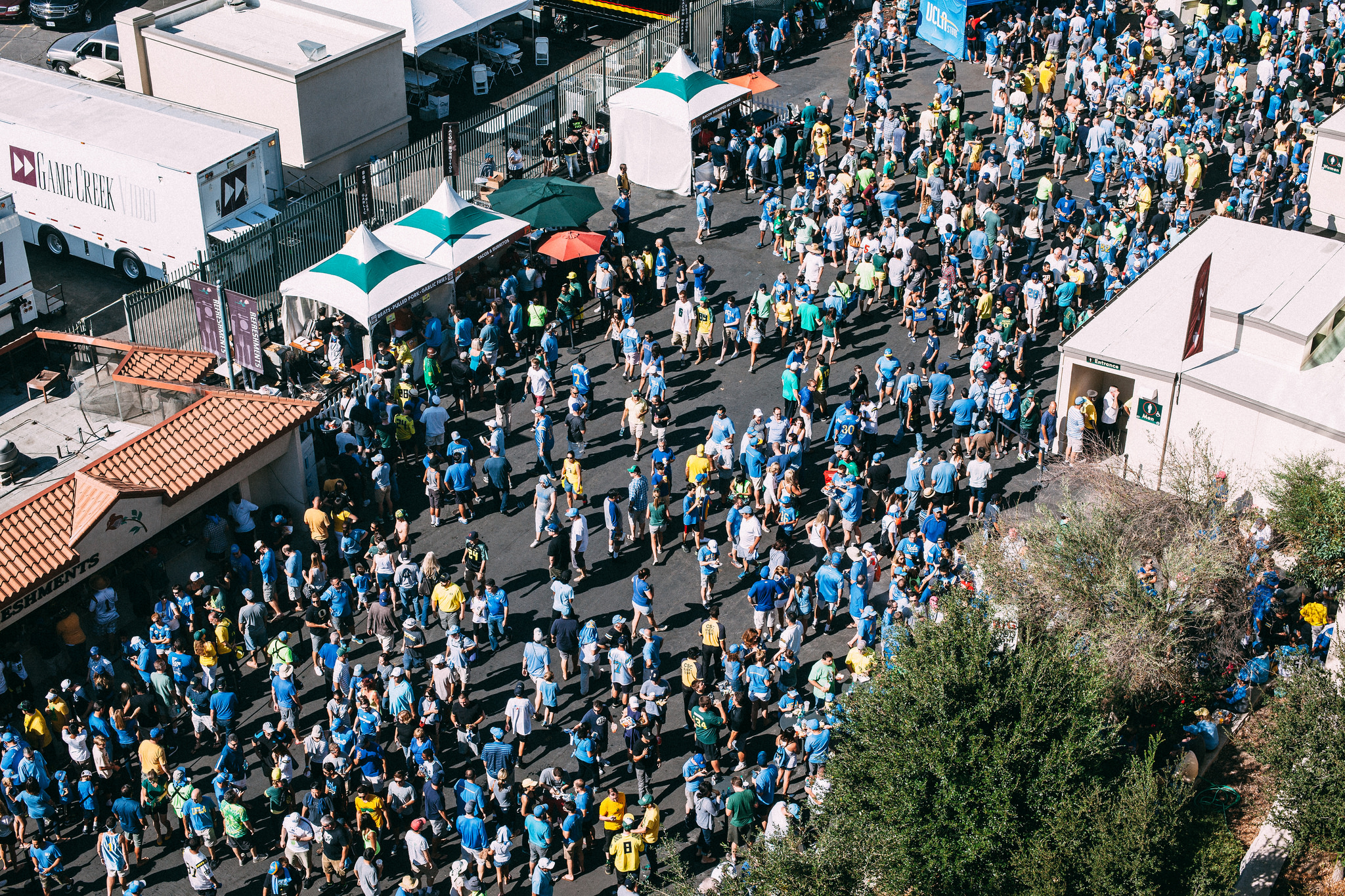 Thousands of college football fans in blue and yellow moving through the outdoor stadium concourse.