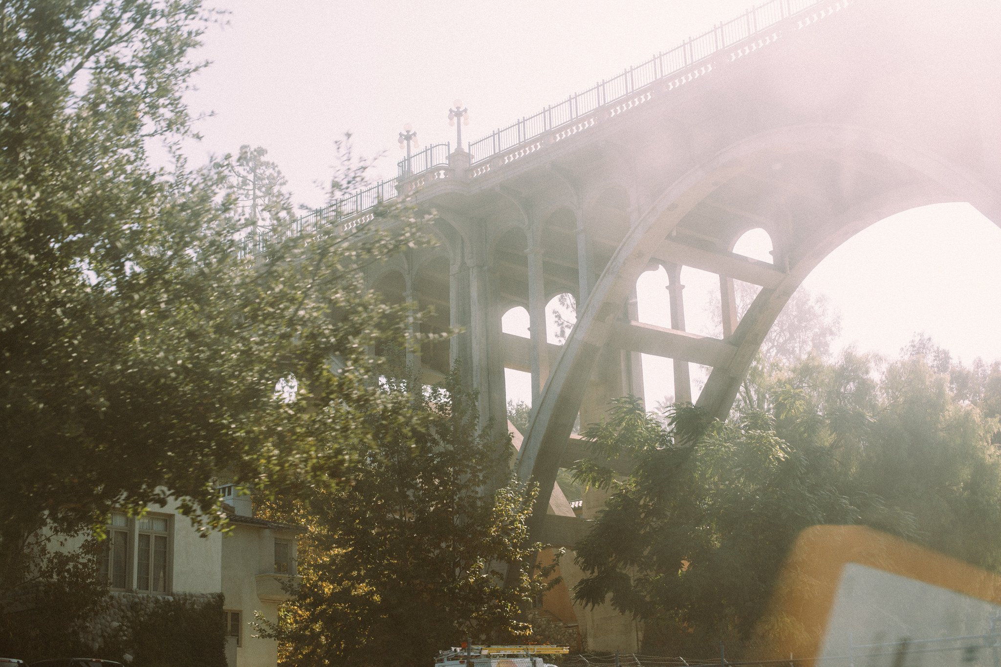 Arches and lamp posts of the Colorado Street Bridge in Pasadena framed by trees in warm sunlight.