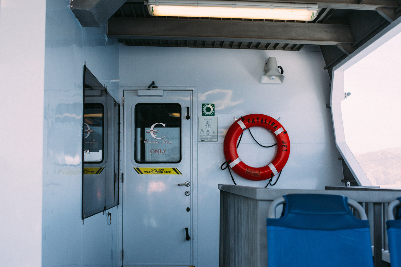 Ferry deck with a red lifebuoy labeled CATALINA JET mounted on a wall beside the Commodore Lounge door.