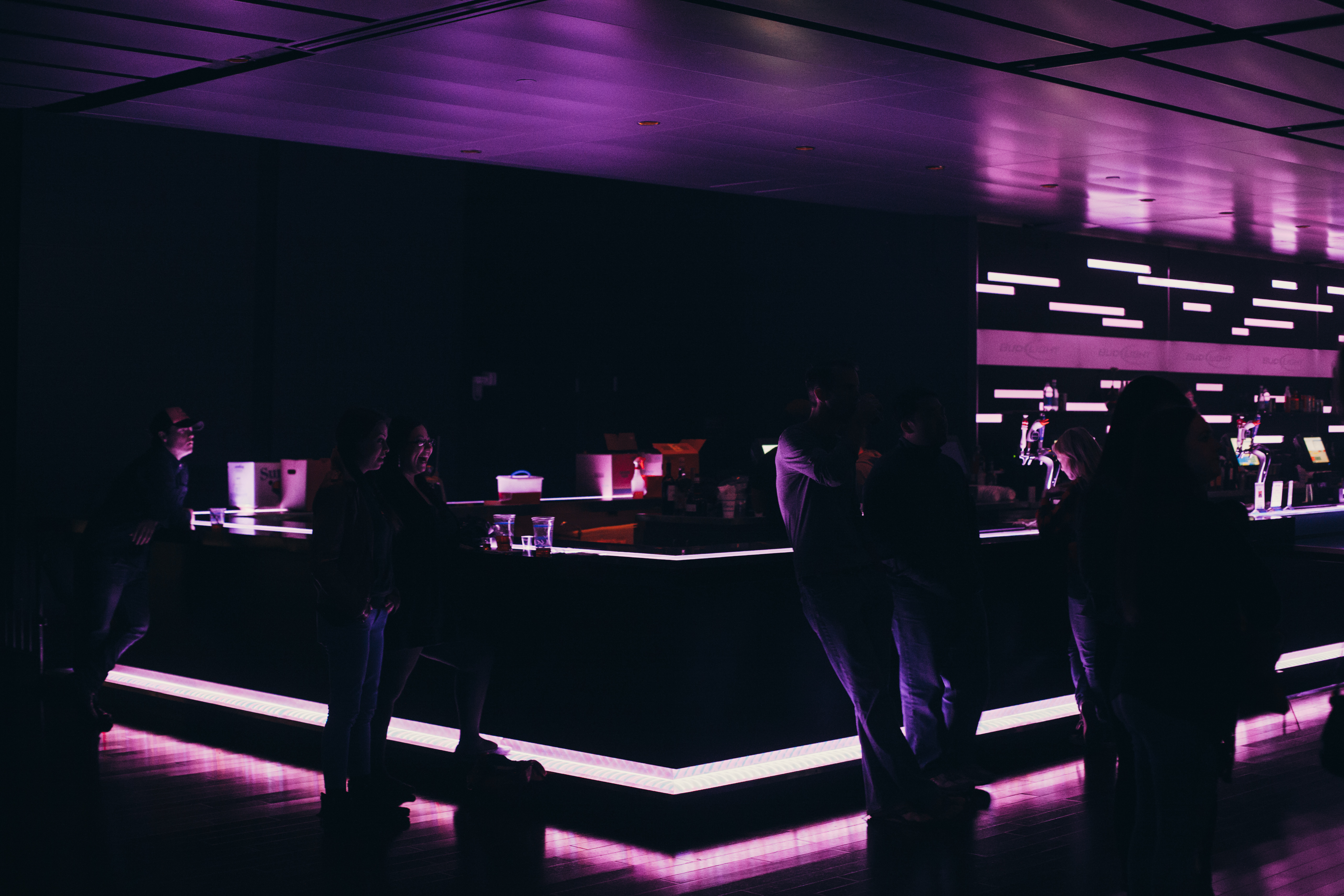 Venue bar illuminated with purple neon lighting as patrons order drinks in the dim ambient interior.