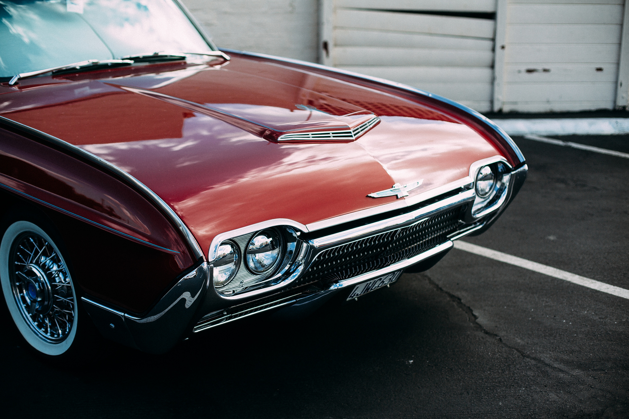 Front angle detail of a vintage burgundy Ford Thunderbird showing its chrome grille, dual headlights, wire wheels, and white wall tires, shot with a Canon 5D Mark II.