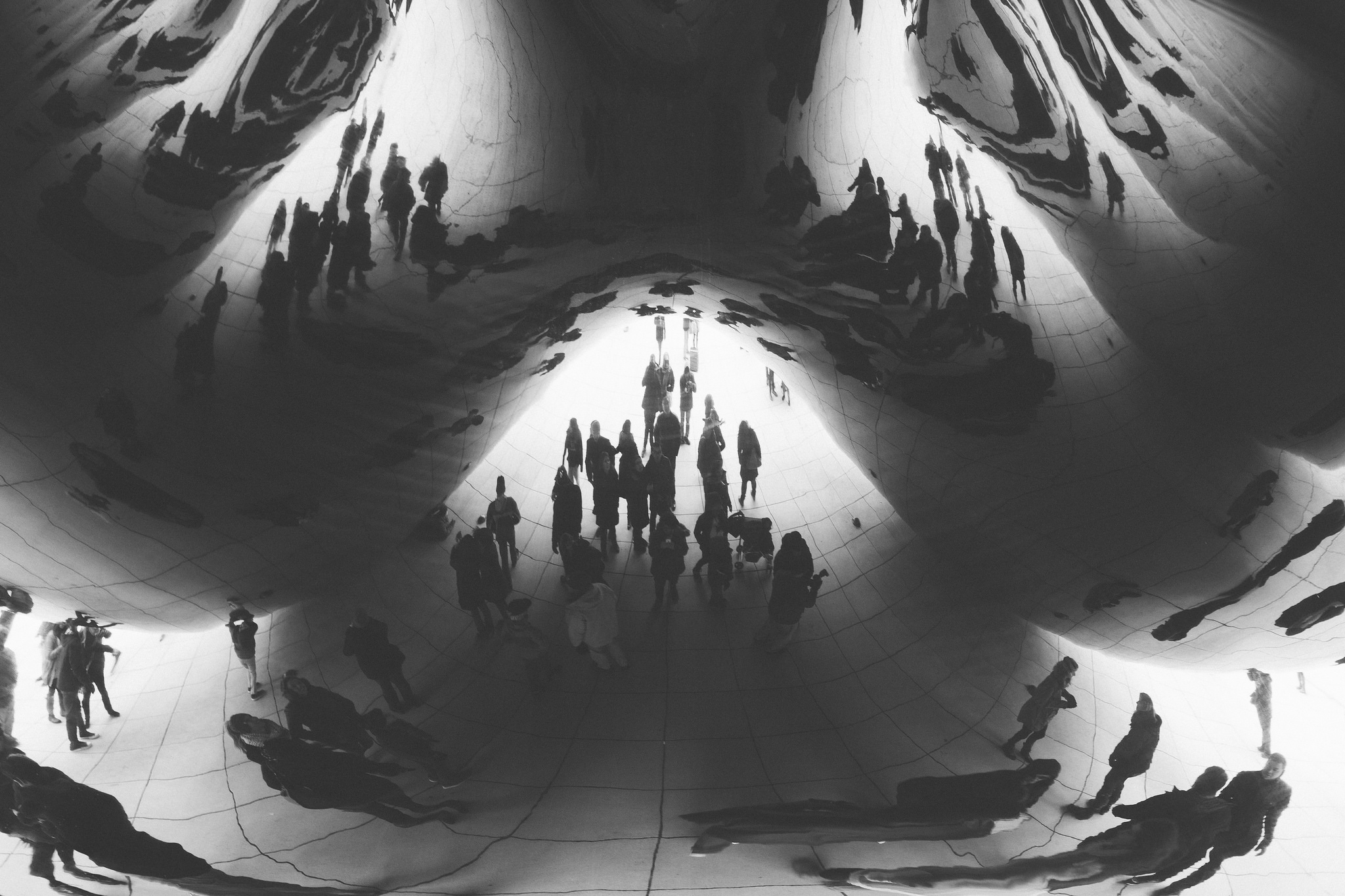 Distorted silhouettes and reflections of crowds under the mirrored underside of Cloud Gate in Chicago.