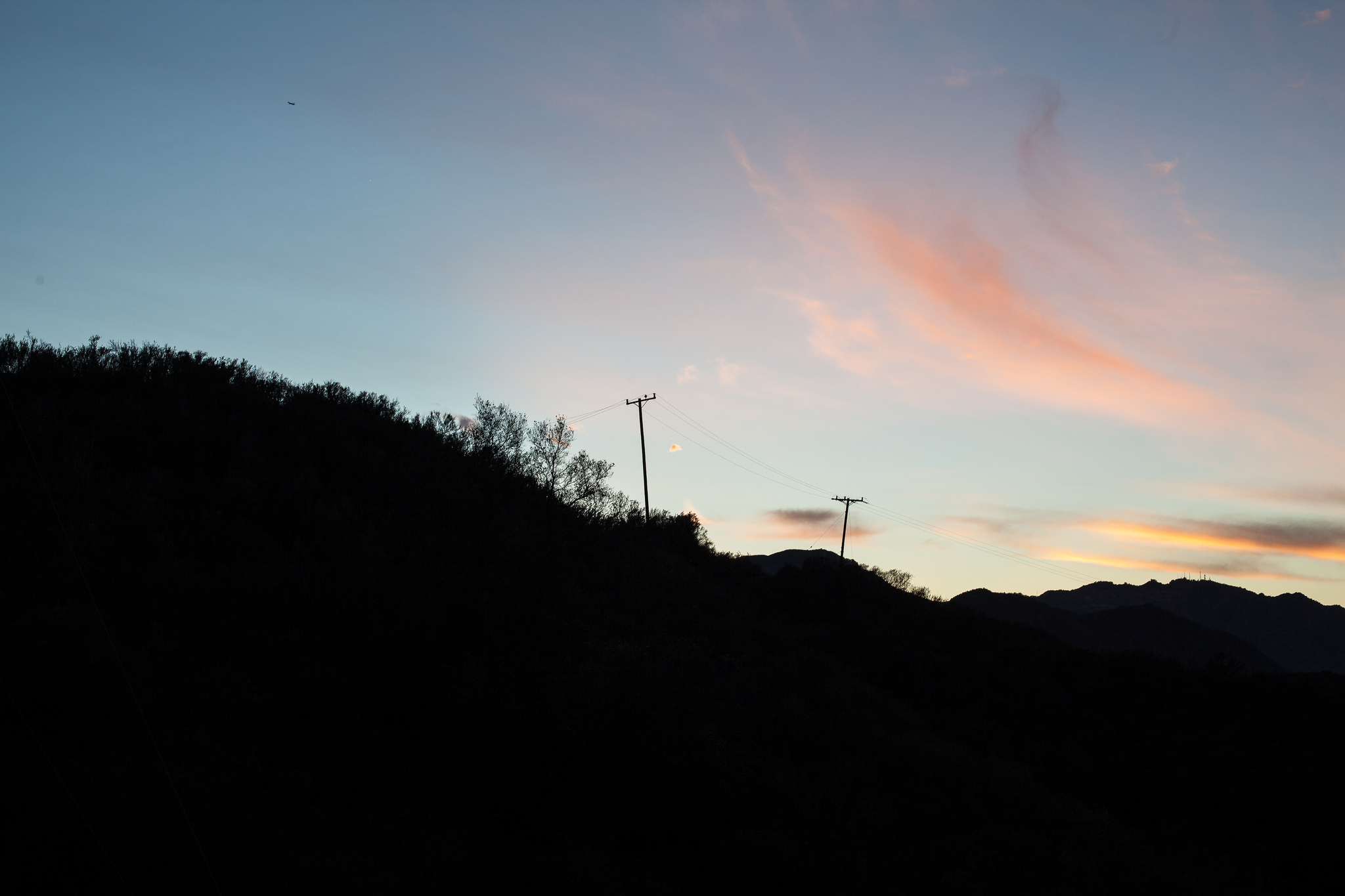 Silhouette of a hillside ridge with utility telephone poles against a blue and peach sunset sky.